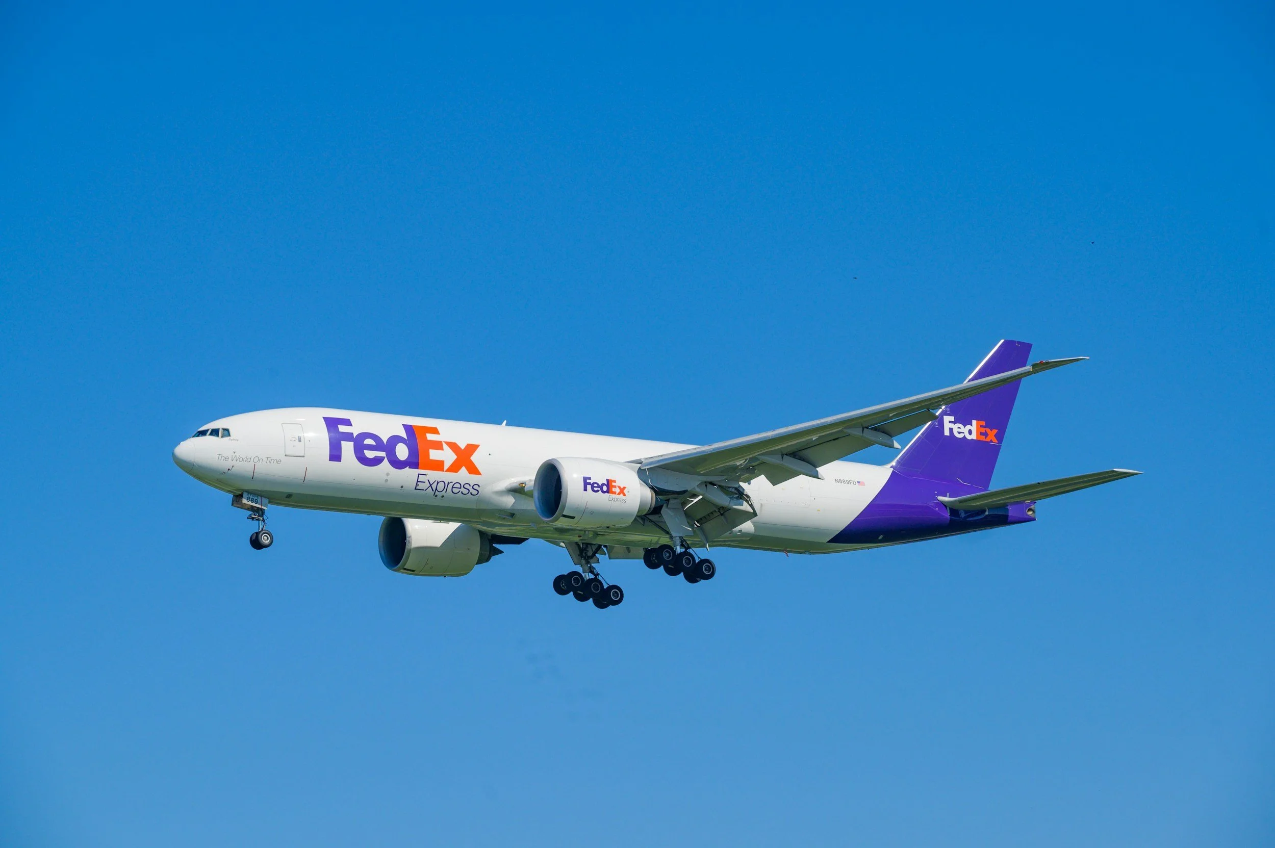 A FedEx Express airplane flying in a clear blue sky with its landing gear extended.