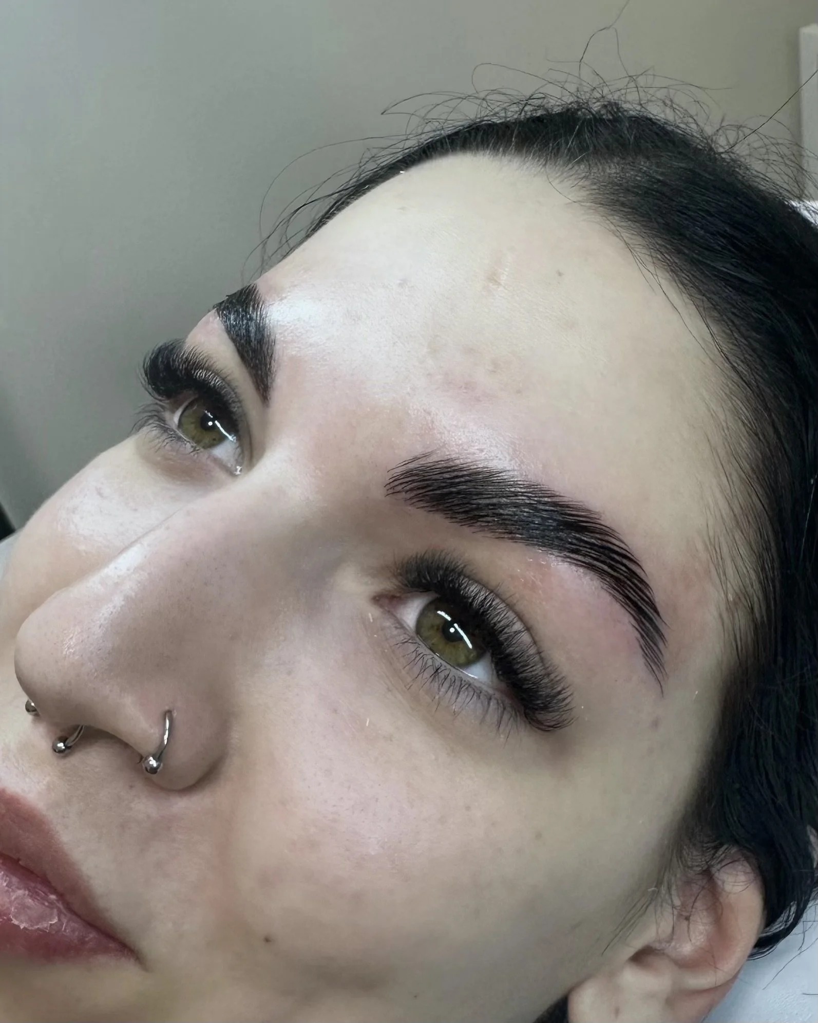 Close-up of a woman's face showing freshly groomed eyebrows, eye makeup, and multiple facial piercings.