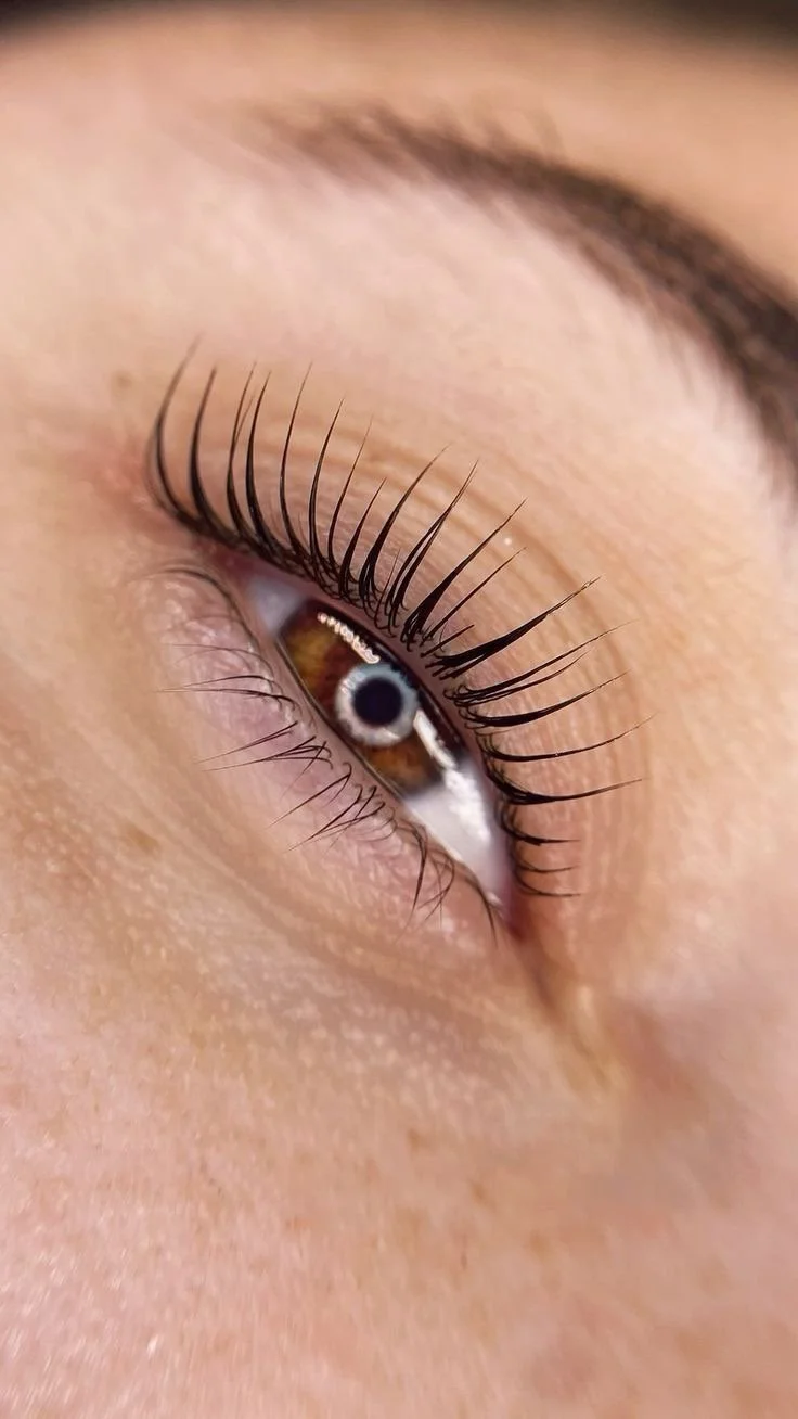 Close-up of a human eye with long eyelashes, brown iris, and surrounding skin.