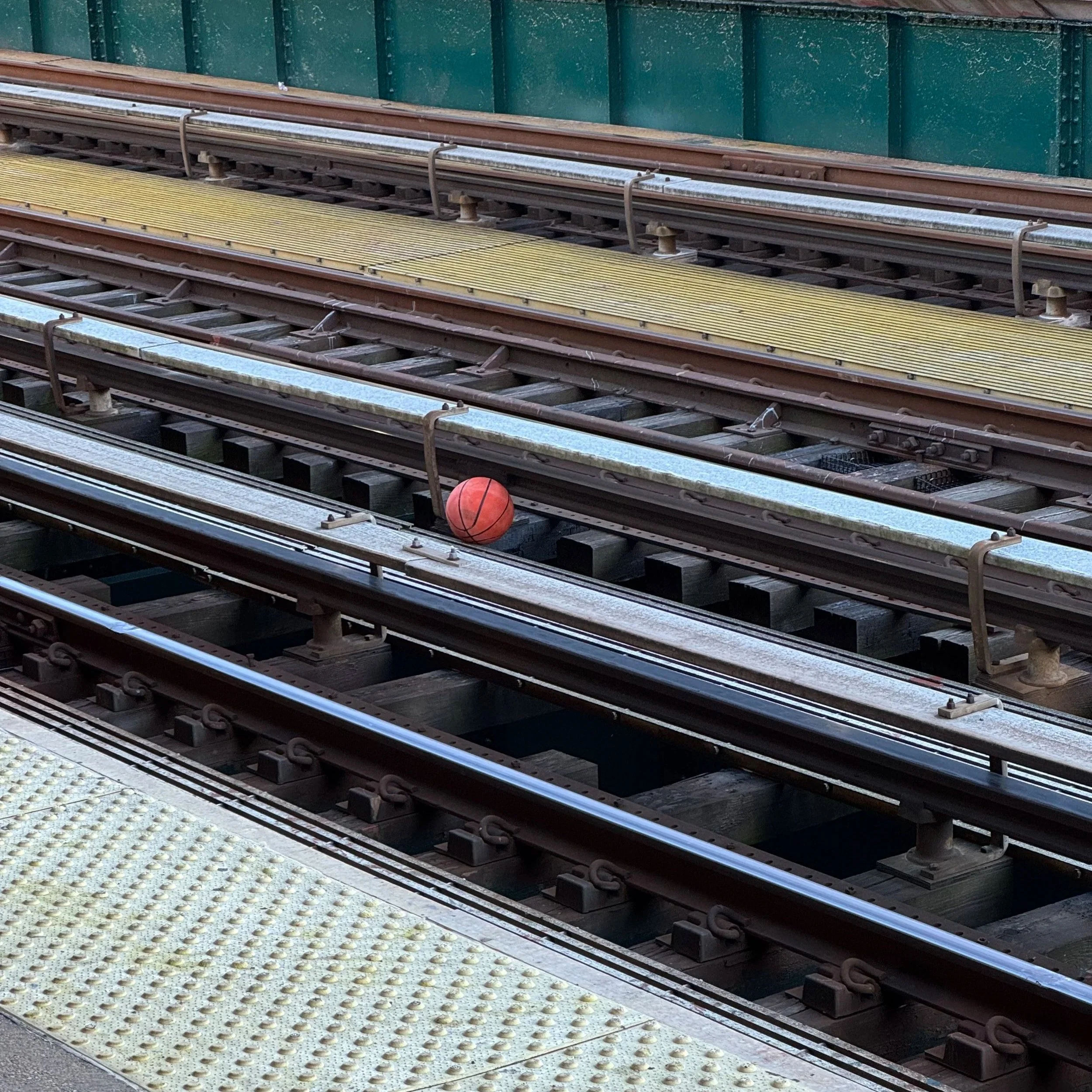 A basketball resting on a railroad track near a yellow safety strip.