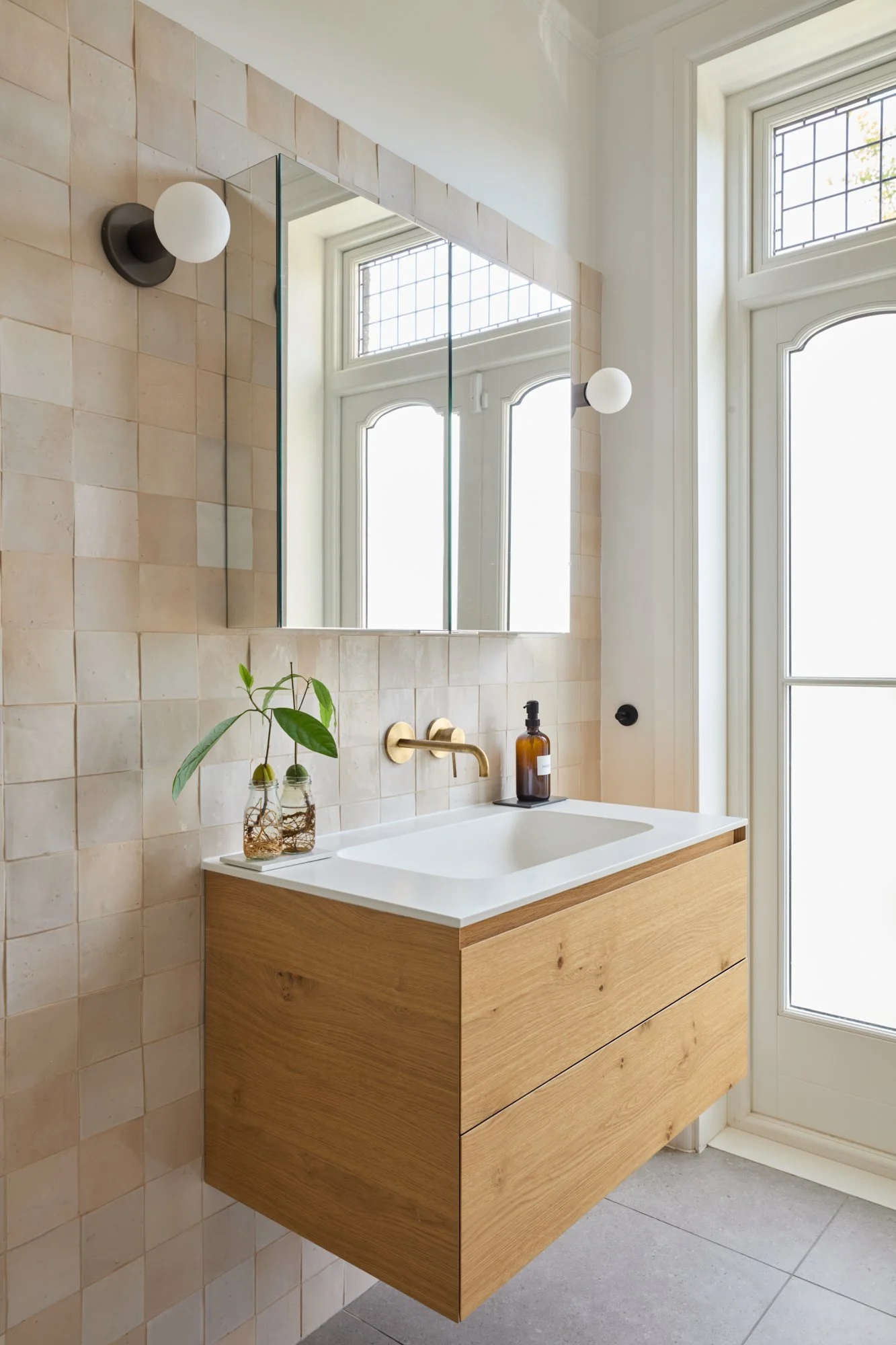 Detail of the floating oak vanity with an integrated Corian sink, paired with brass wall-mounted taps. The soft sheen of zellige tiles creates a textured, timeless backdrop that balances elegance with everyday functionality.