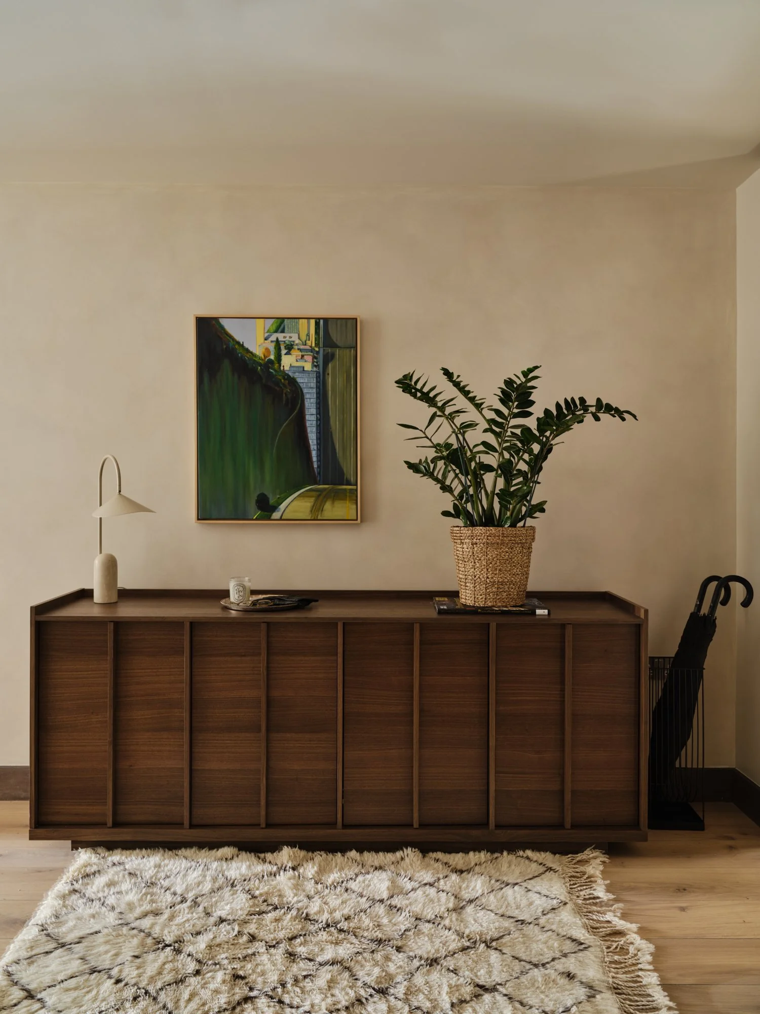 Warm, material-led hallway featuring a large walnut sideboard, moroccan berber rug and oak flooring in a Fulham home. Walls are lime washed.