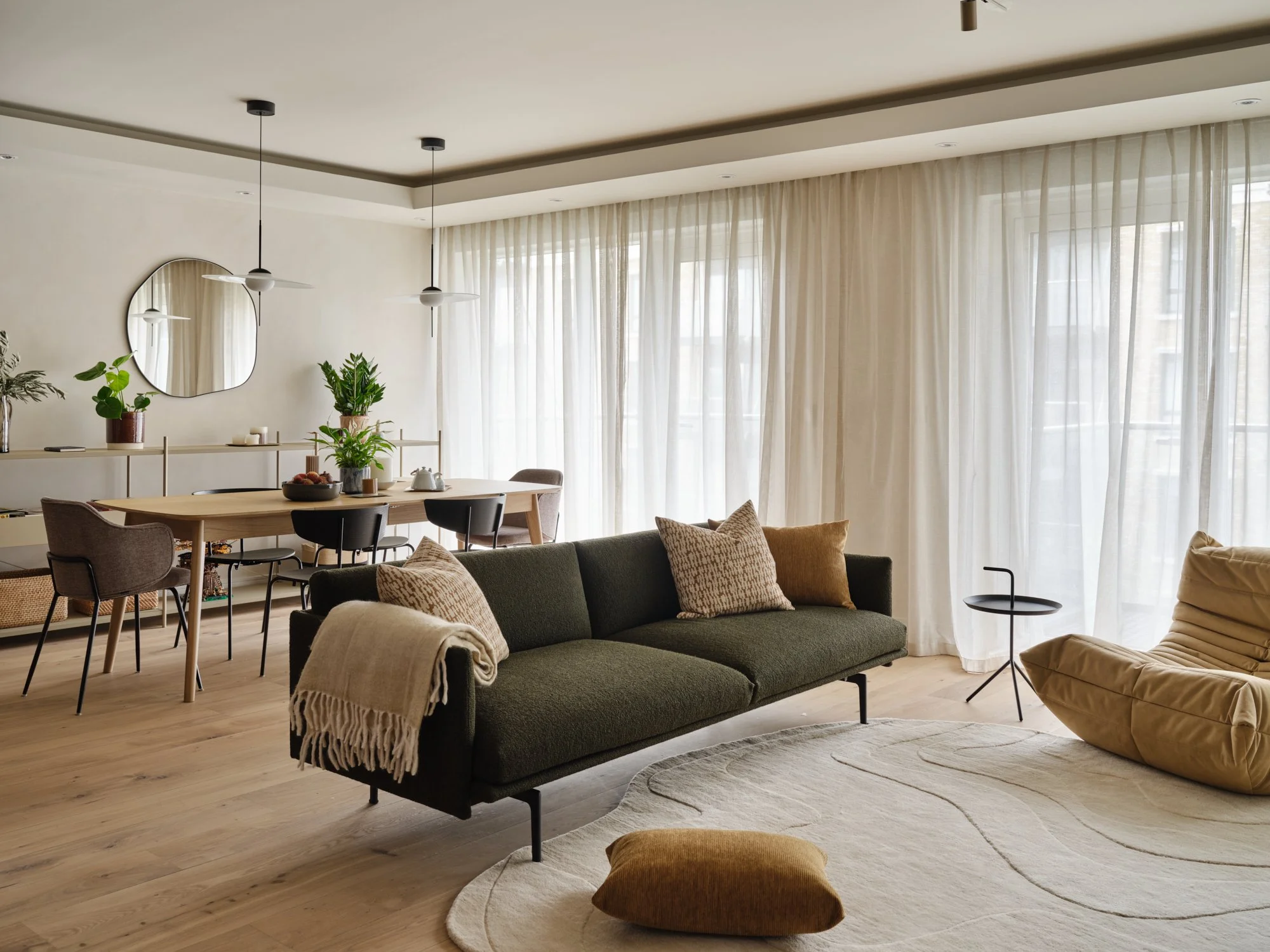 Open-plan living and dining area with bespoke joinery, soft furnishings and sheer curtains in a West London family home.