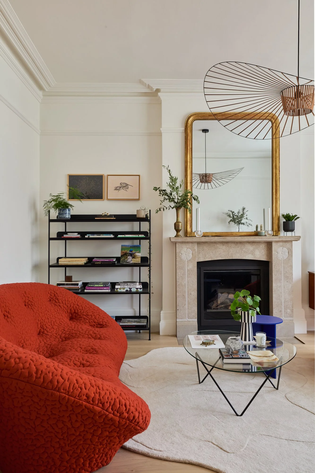 Parisian-inspired formal reception room with high ceilings and large windows, styled with a Louis Philippe mirror, statement pendant, and French post-modern orange sofas. The design blends Haussmannian elegance with Scandinavian and mid-century moder