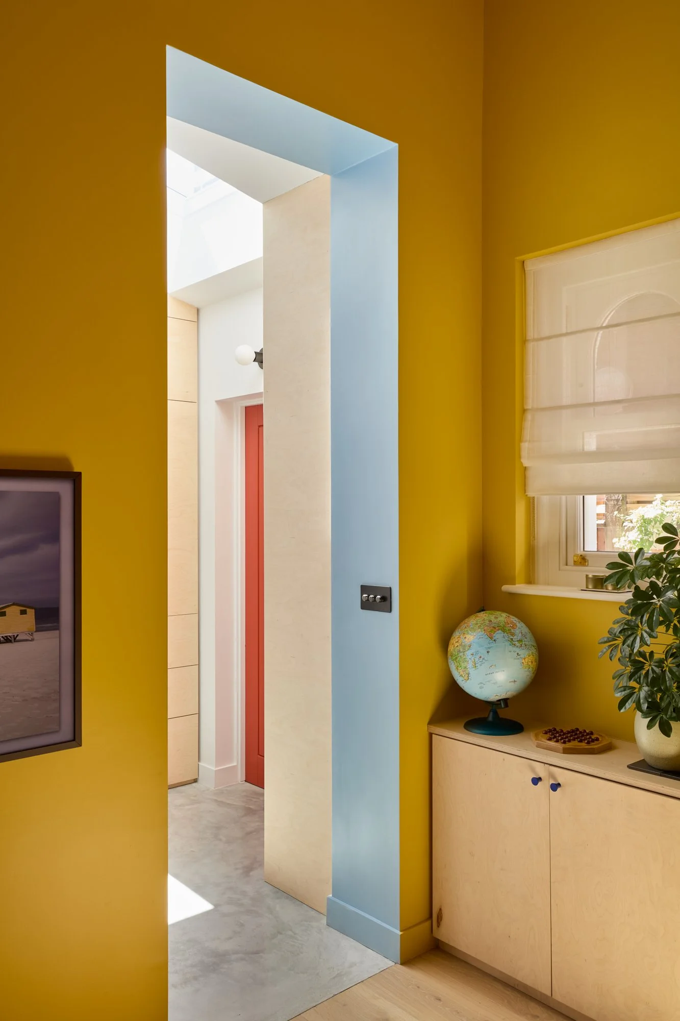 Vibrant playroom and family room with yellow, red, and blue accents. Features a chimney breast desk nook, bespoke birch plywood joinery, PH5 pendant, stripy sofa, jute rug, and decorative plants for a playful yet functional space.