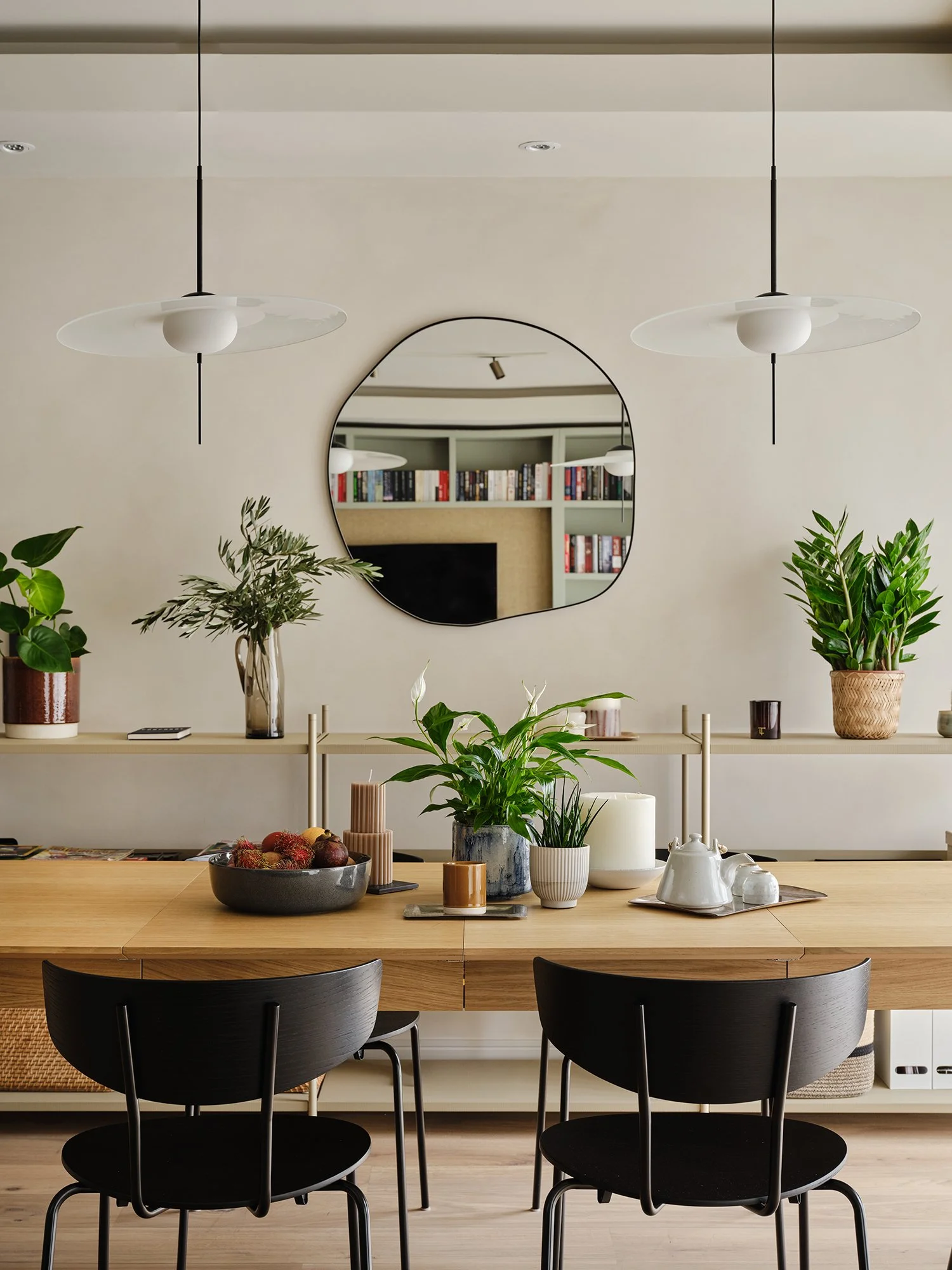 Dining area with sculptural pendant lighting, oak table and organic mirror against the lime washed wall in a contemporary West London apartment.