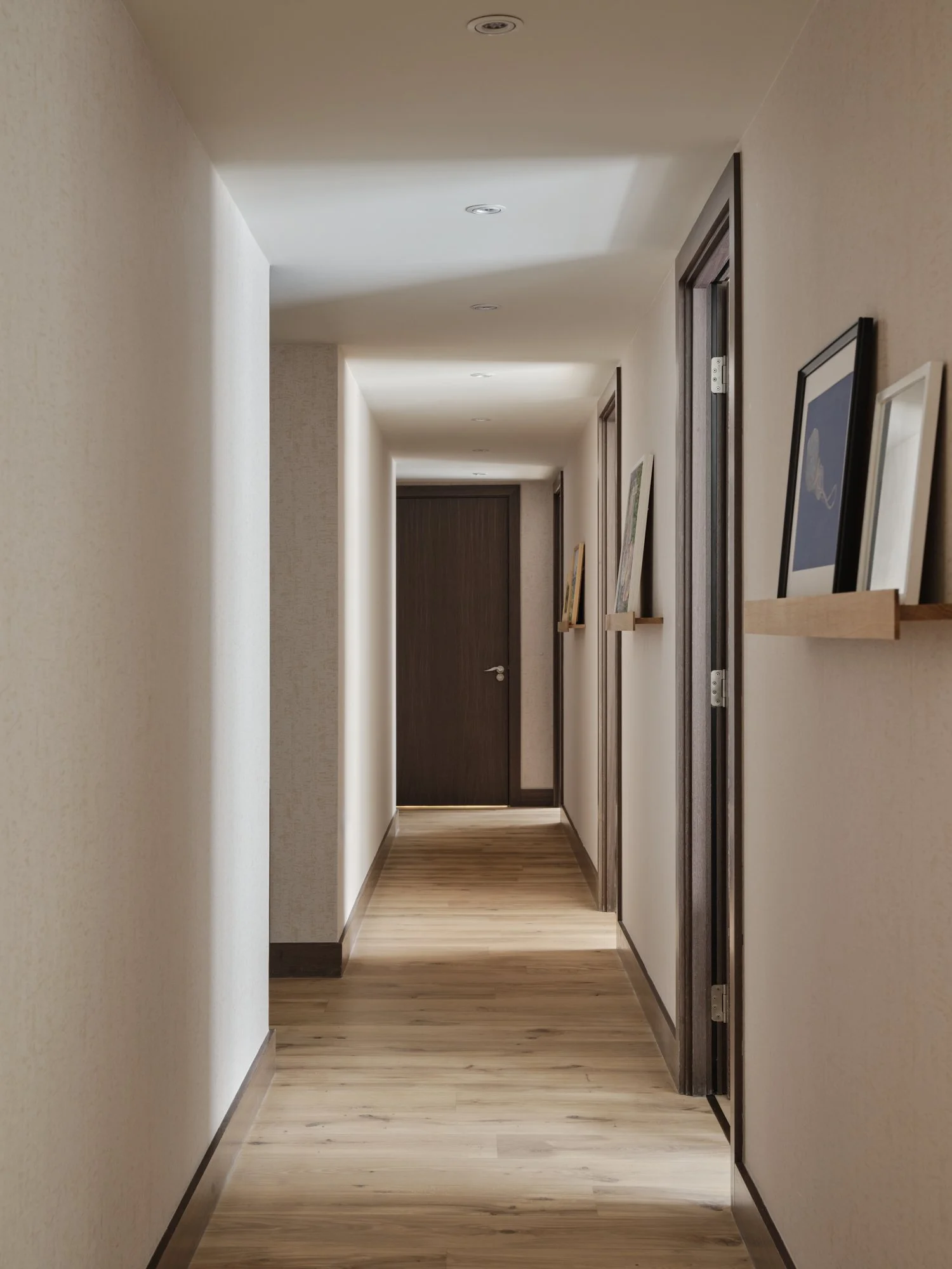 Corridor with textured walls transformed into a home art gallery with picture ledges, warm lighting and oak flooring in a Fulham Reach apartment.