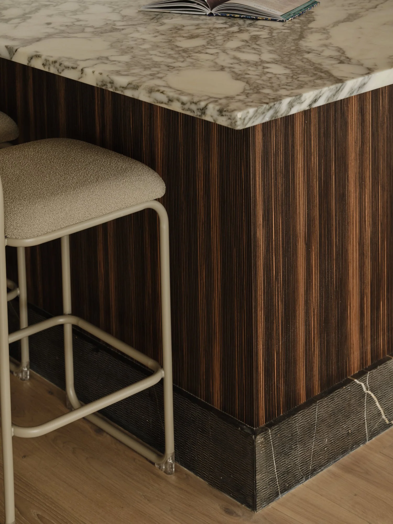 Detail of kitchen peninsula with ribbed ebony veneer, Arabescato marble worktop and upholstered bar stool in a Fulham Reach home.