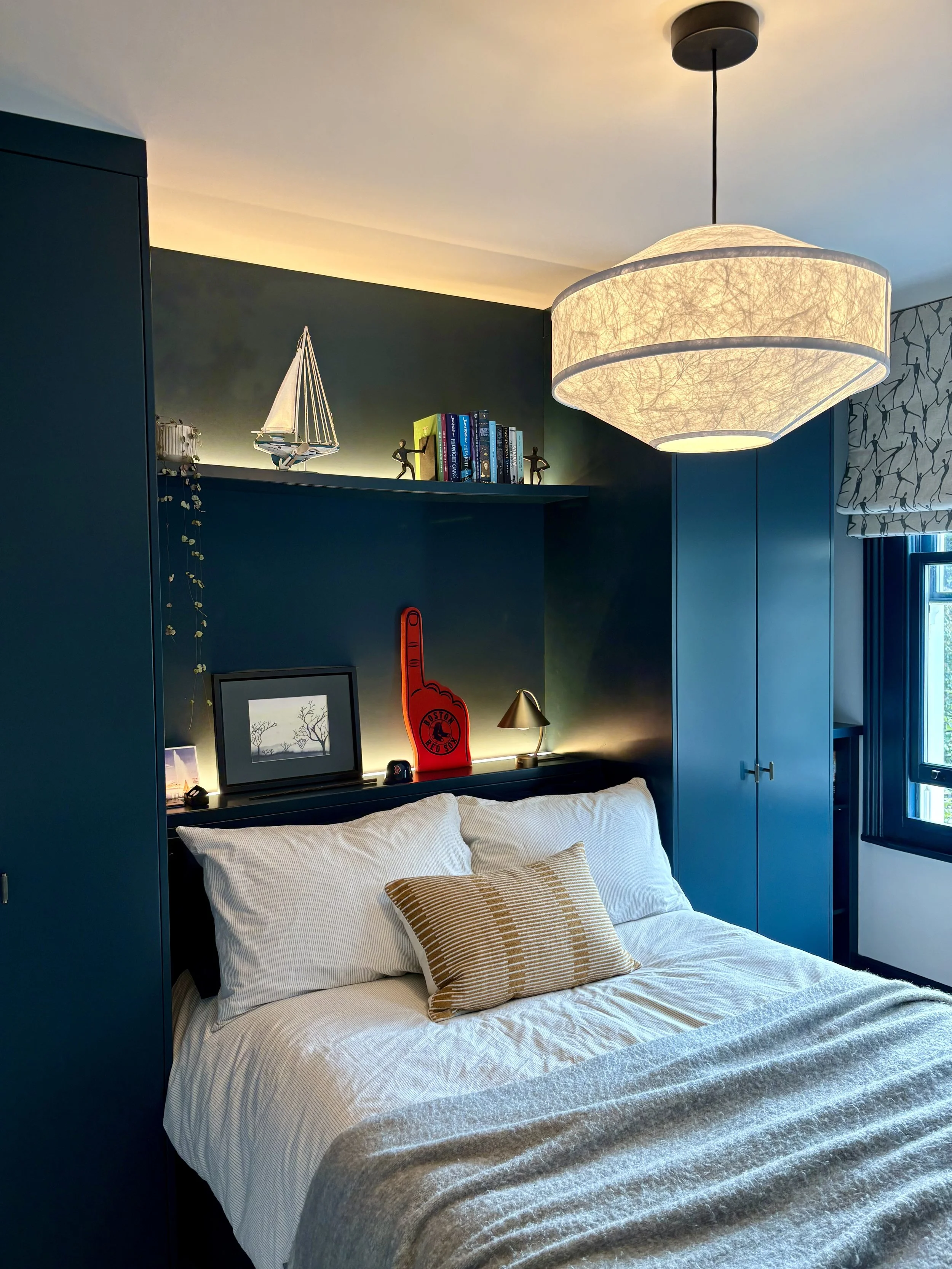 Modern teen bedroom in Clapham featuring bespoke dark blue fitted wardrobes, a recessed headboard with integrated shelving and LED lighting, and a large statement pendant.