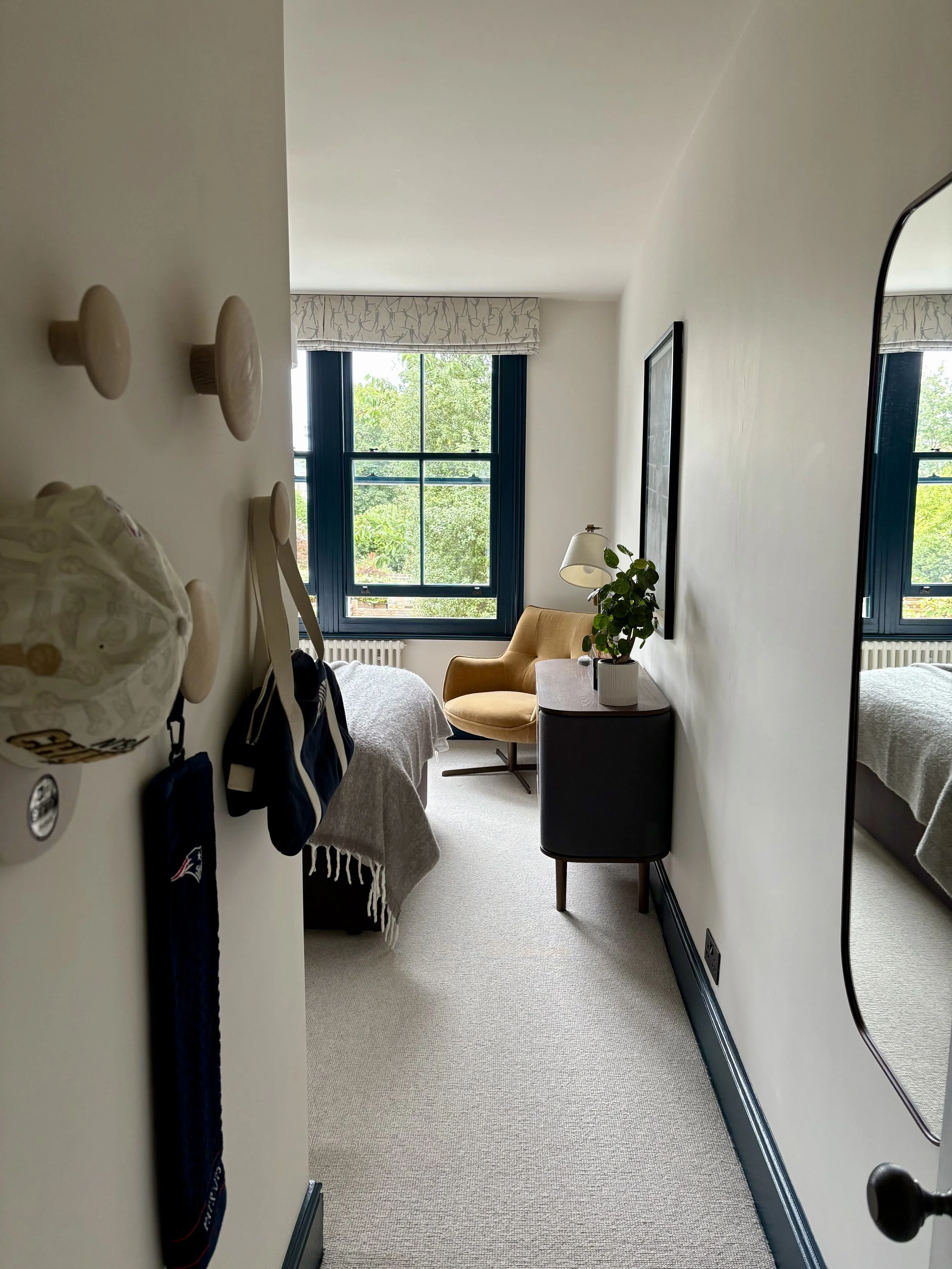 Stylish teen bedroom redesign in Clapham with bespoke joinery, a bold blue feature wall, sports-themed artwork, and a cosy reading corner with an accent chair.