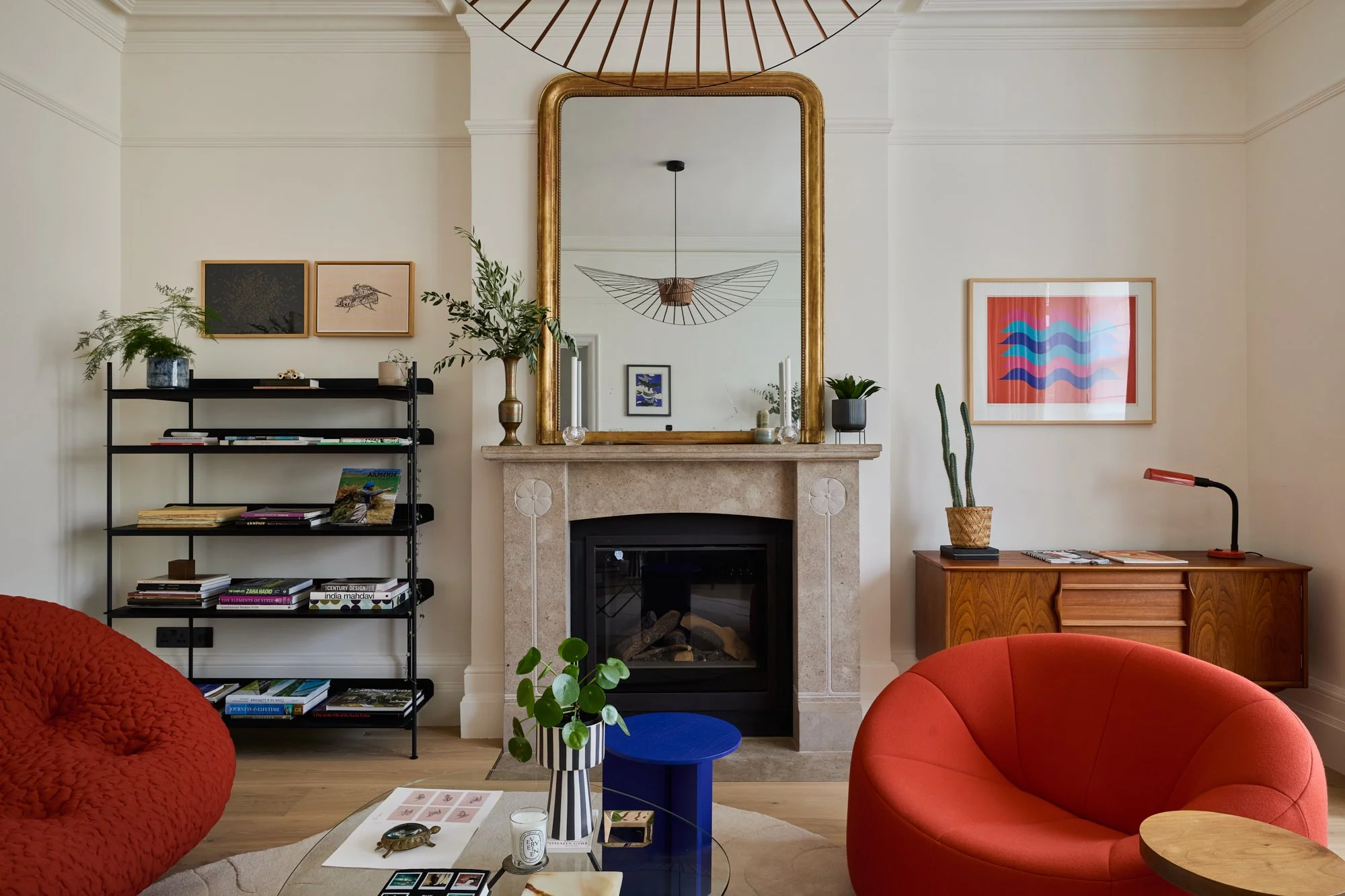 Parisian-inspired formal reception room with high ceilings and large windows, styled with a Louis Philippe mirror, statement pendant, and French post-modern sofas. The design blends Haussmannian elegance with Scandinavian and mid-century modern piece