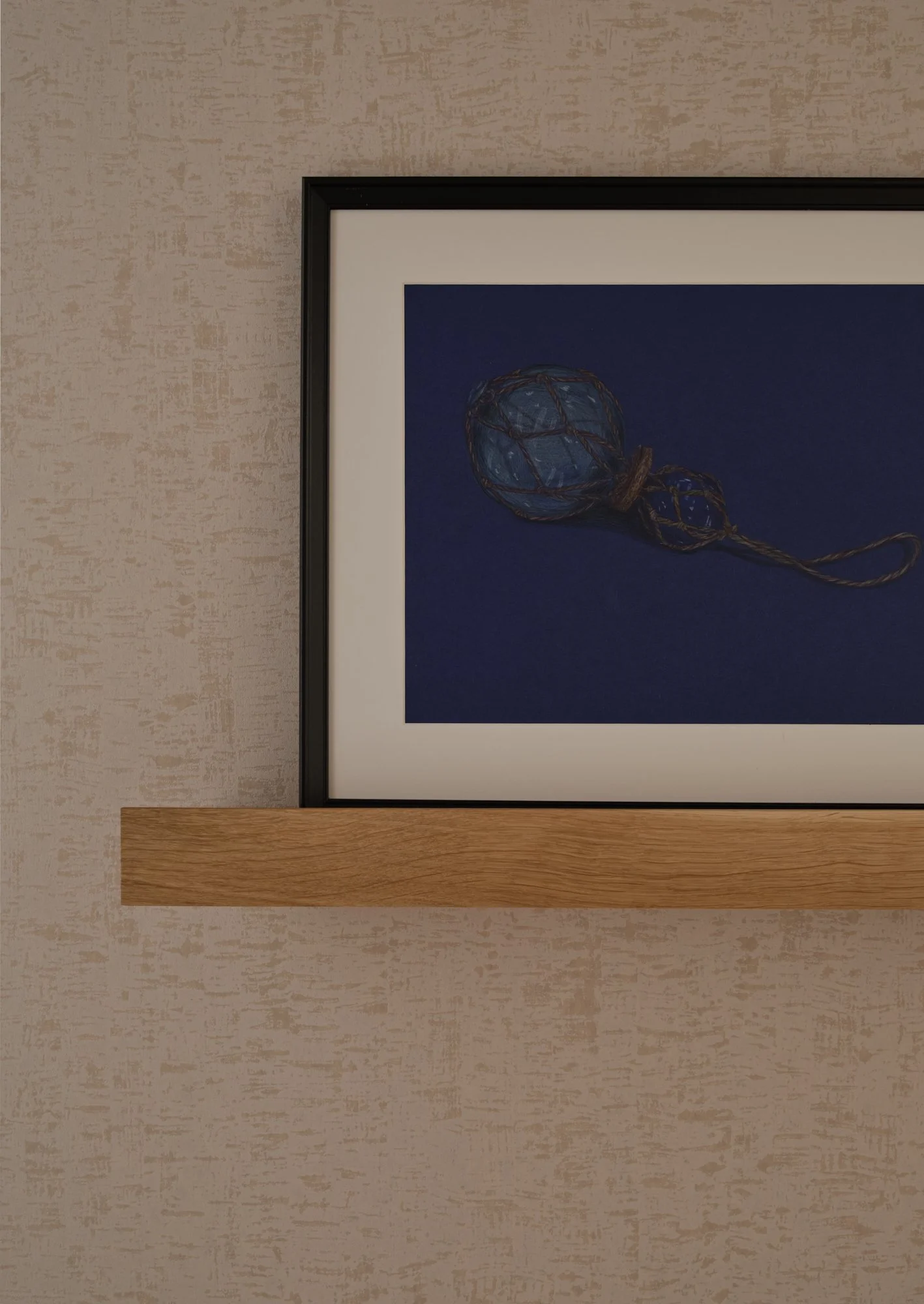 Framed artwork displayed on an oak picture ledge within a textured wallpapered corridor in a Fulham Reach apartment.