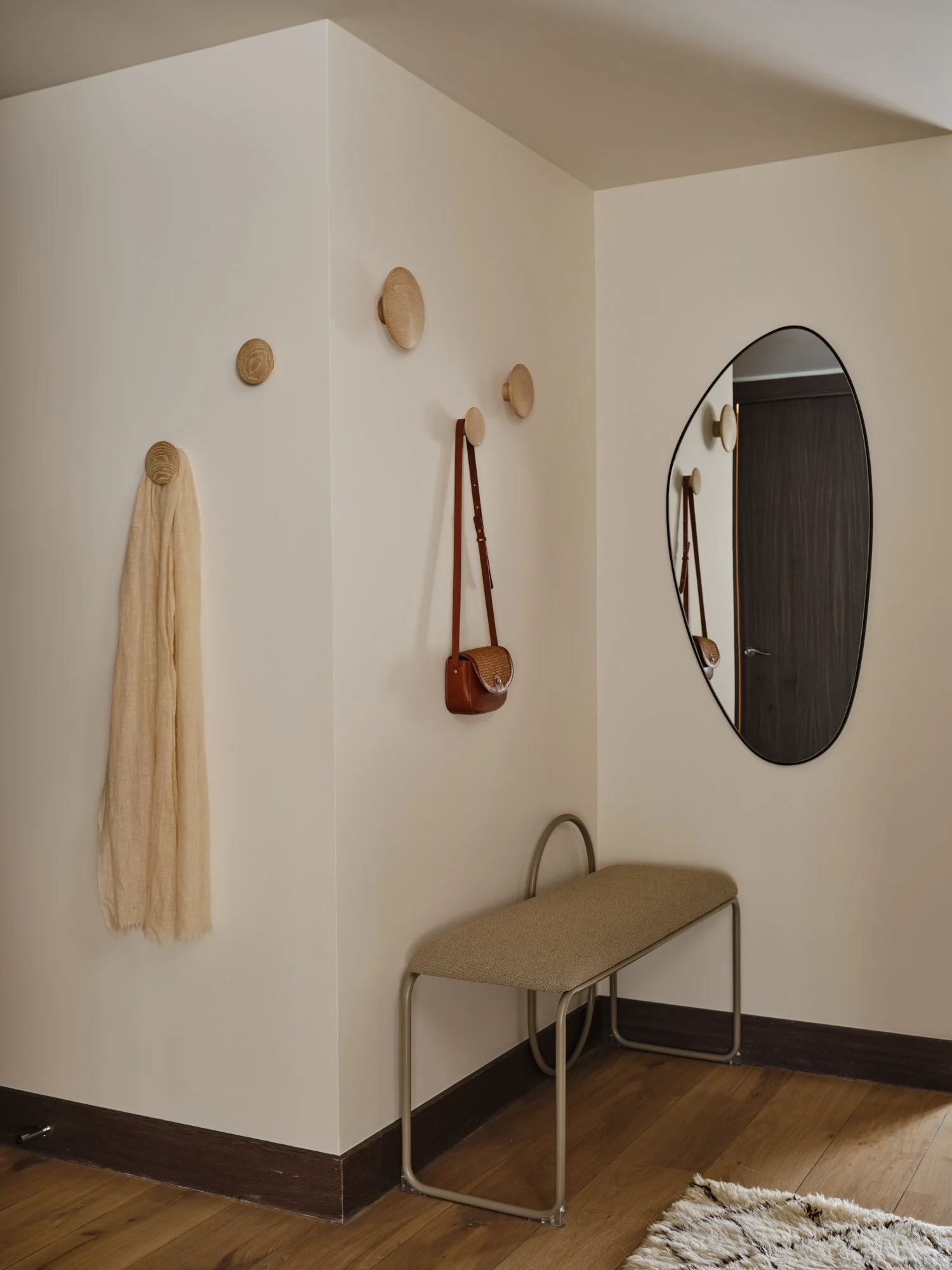 Minimalist hallway design in Fulham Reach, West London, featuring an upholstered bench, wooden wall hooks and an organic-shaped mirror.