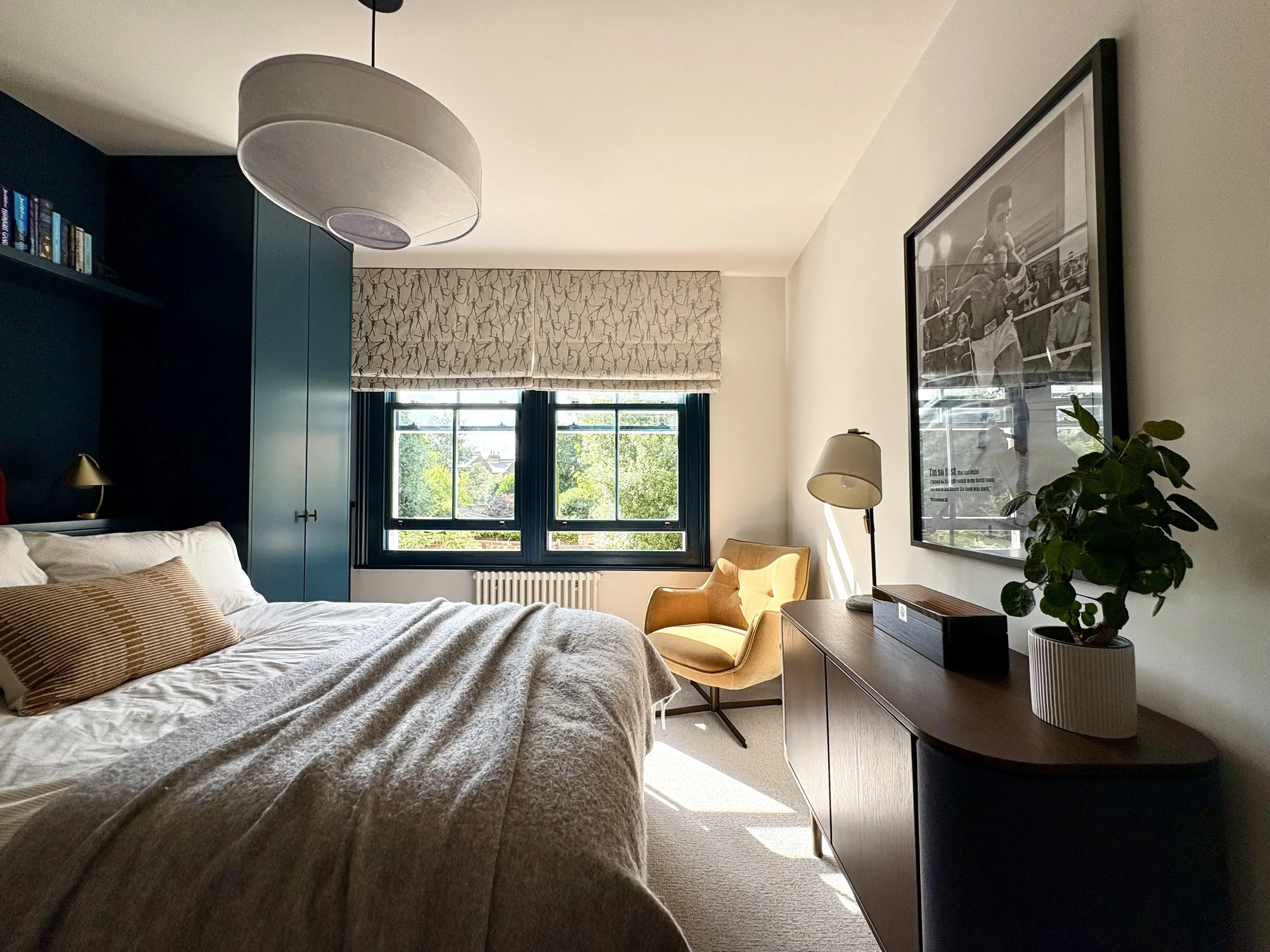 Stylish teen bedroom redesign in Clapham with bespoke joinery, a bold blue feature wall, sports-themed artwork, and a cosy reading corner with an accent chair.