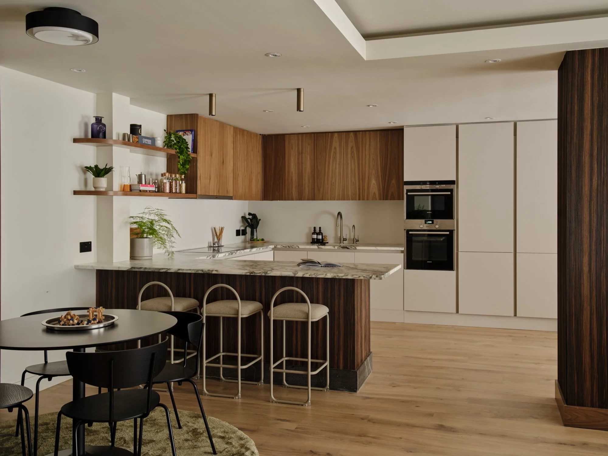 Eco-conscious kitchen design in Fulham Reach, West London, featuring walnut cabinetry, Arabescato marble worktops and peninsula seating.
