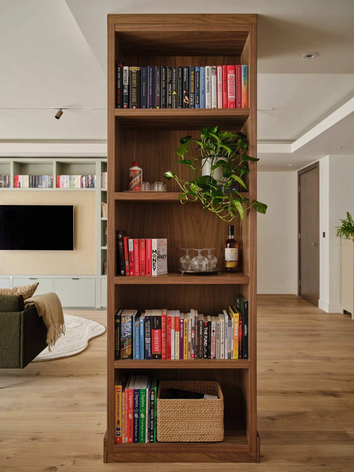 Bespoke walnut bookshelf and bar unit concealing a structural column, used as a room divider between kitchen and living space in a Fulham Reach apartment.