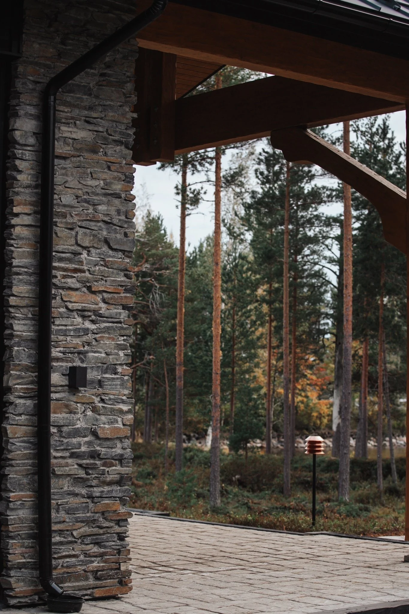 Stone-walled house section with wooden roof and forest landscape, part of a secluded eight-bedroom luxury residence designed for privacy and calm.