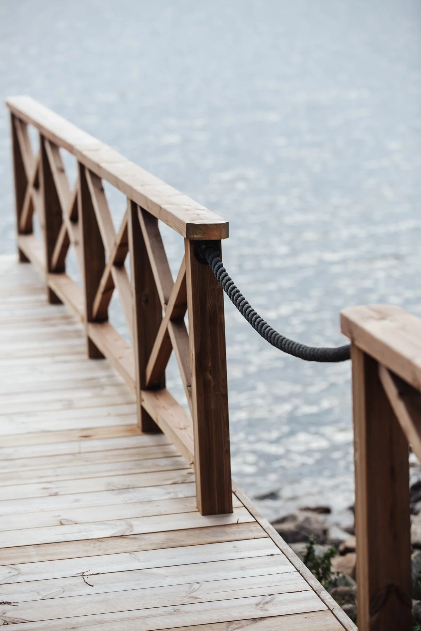Wooden dock with black rope railing on a clear Finnish lake, reflecting the serene privacy and exclusivity of the retreat’s forest surroundings.