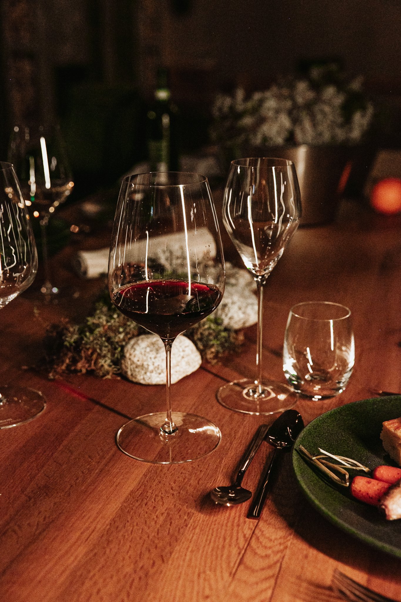 A person pouring red wine sauce over a plate with beef, vegetables, and bread in a dimly lit setting.