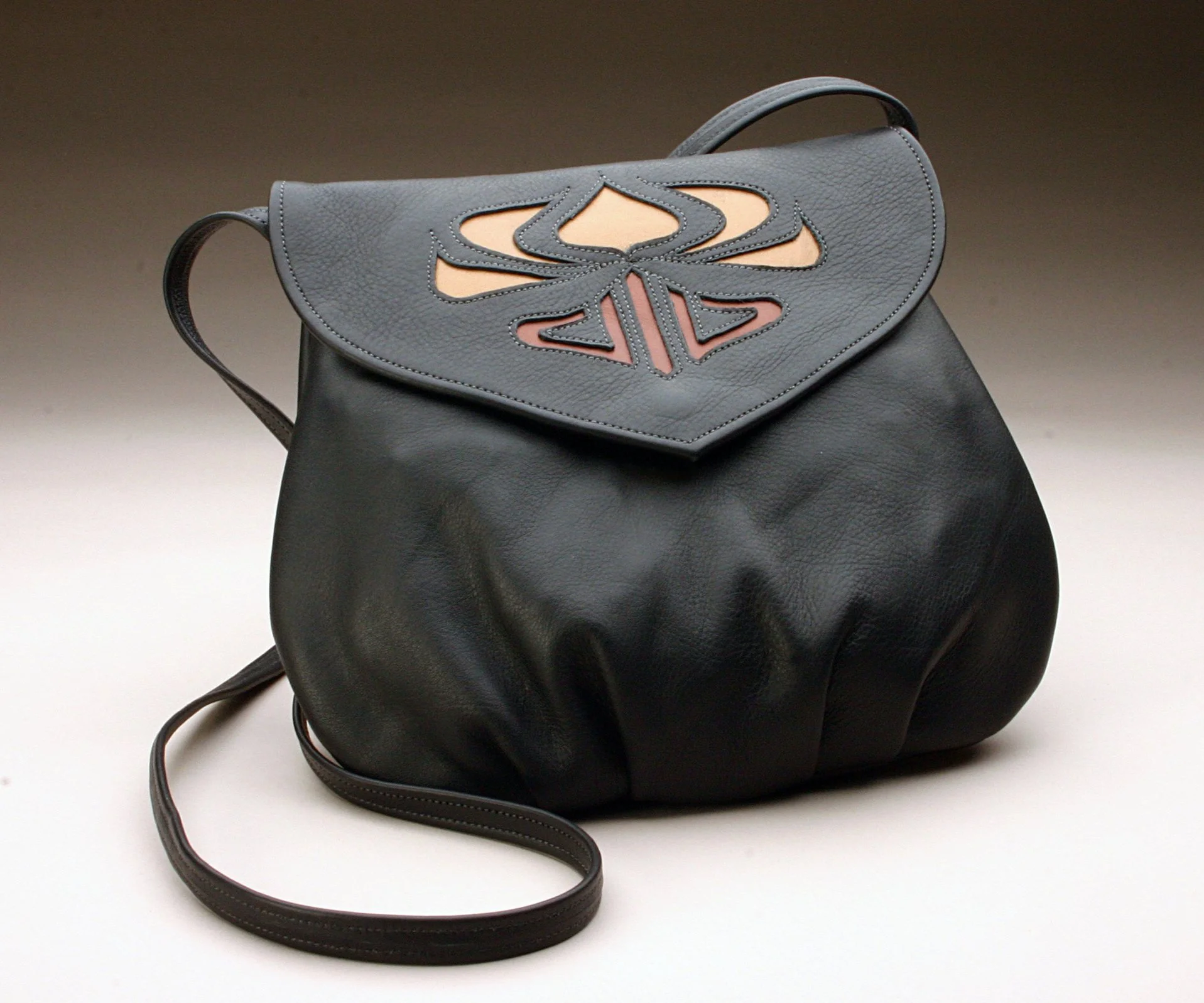 A black leather handbag with a flap featuring a multicolored butterfly design in shades of pink, beige, and black, on a plain light background.