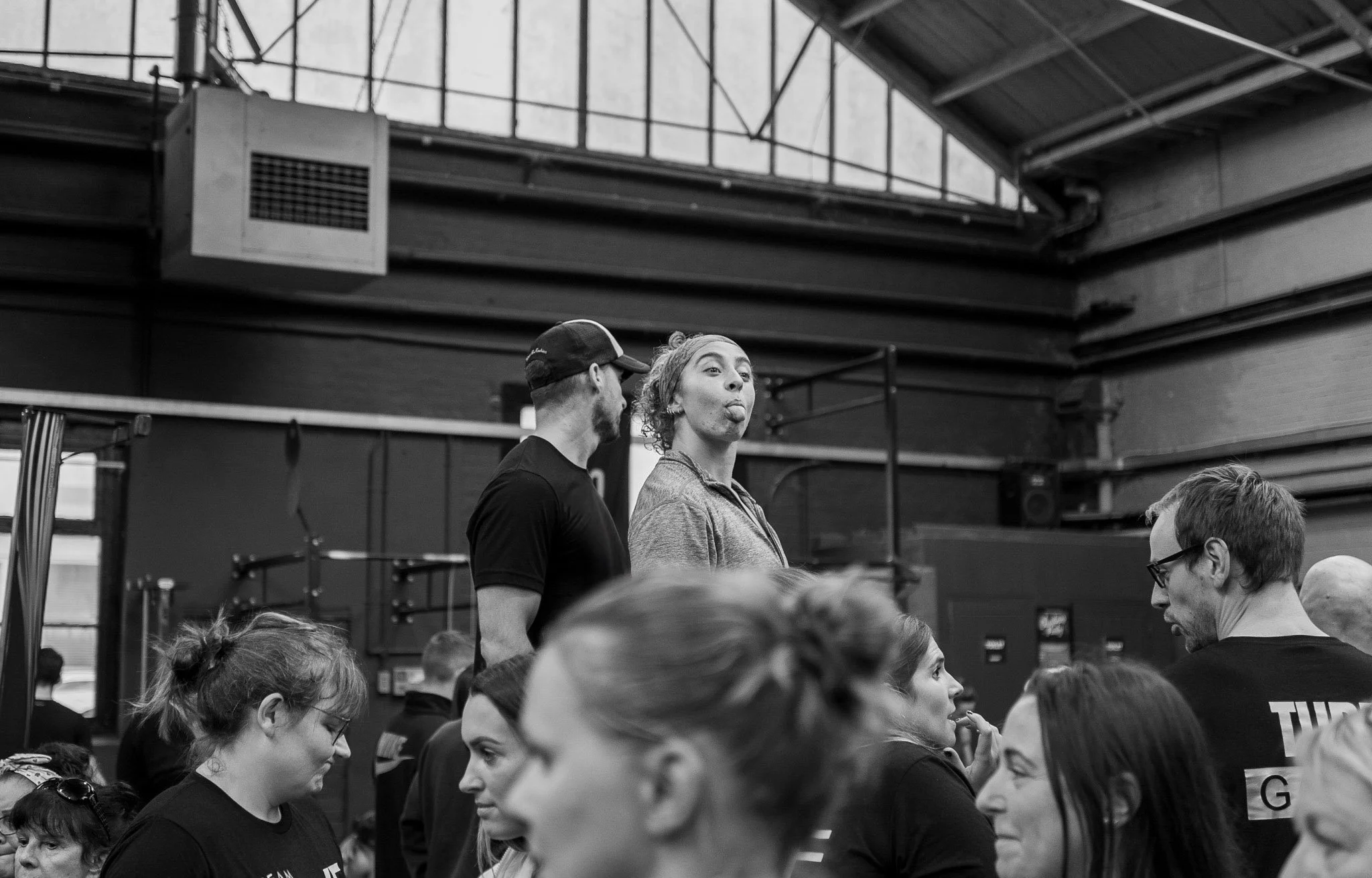 Black and white image inside of the shed of a large group of people and a woman having fun in a large group at an event