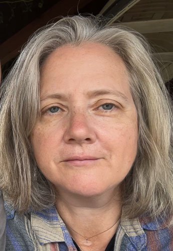 Close-up of a woman with shoulder-length gray hair, light skin, and blue eyes.