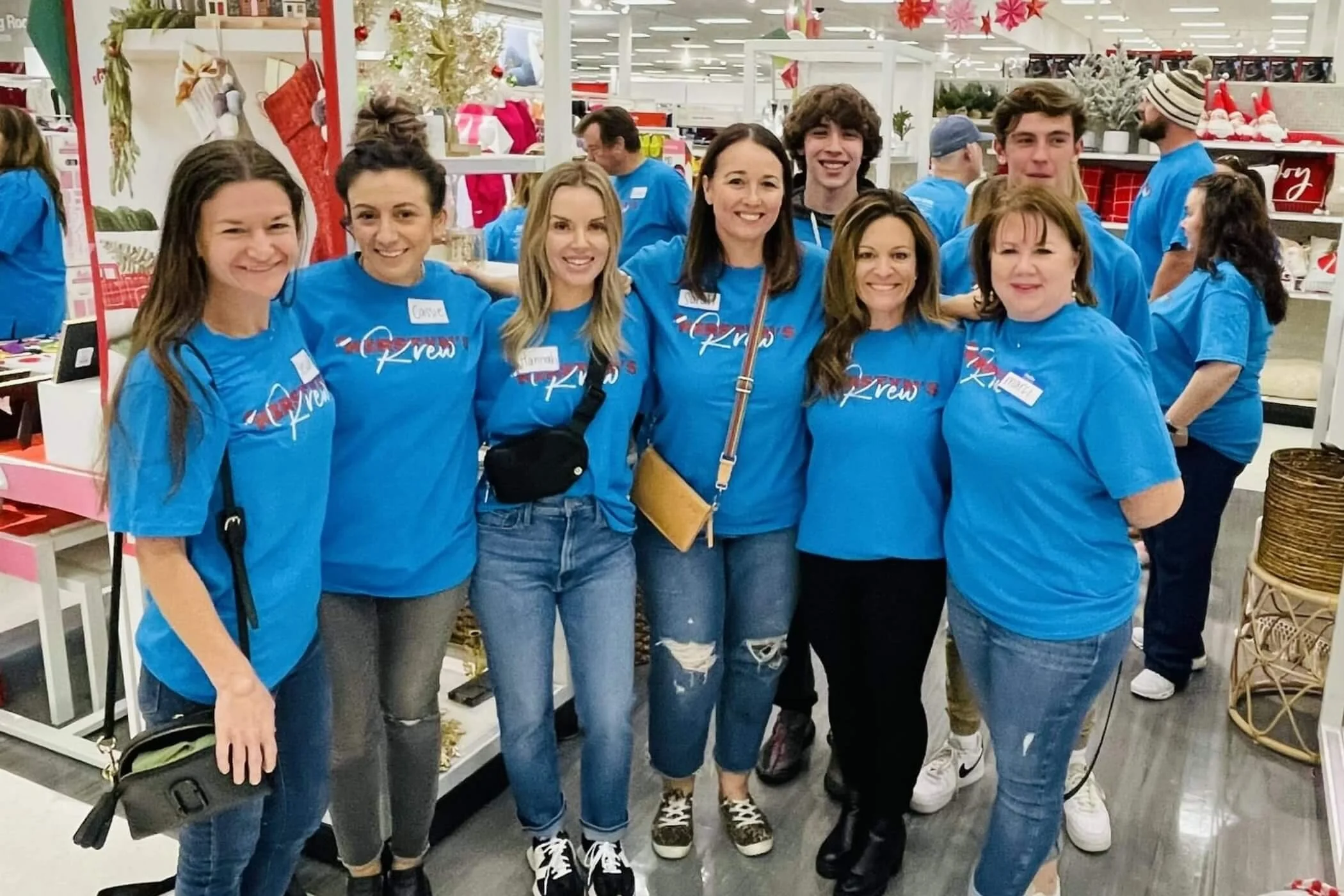 Group of eight people wearing matching blue shirts with 'Krew' logo, standing in a store decorated for Christmas.