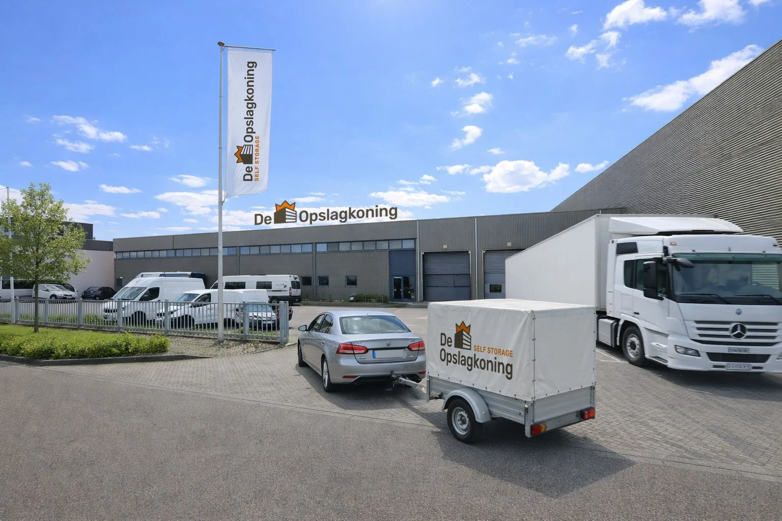Warenhuis met de naam 'De Opslagkoning', een parkeerplaats met meerdere voertuigen, waaronder een vrachtwagen en een auto, en een vlag met de bedrijfsnaam.