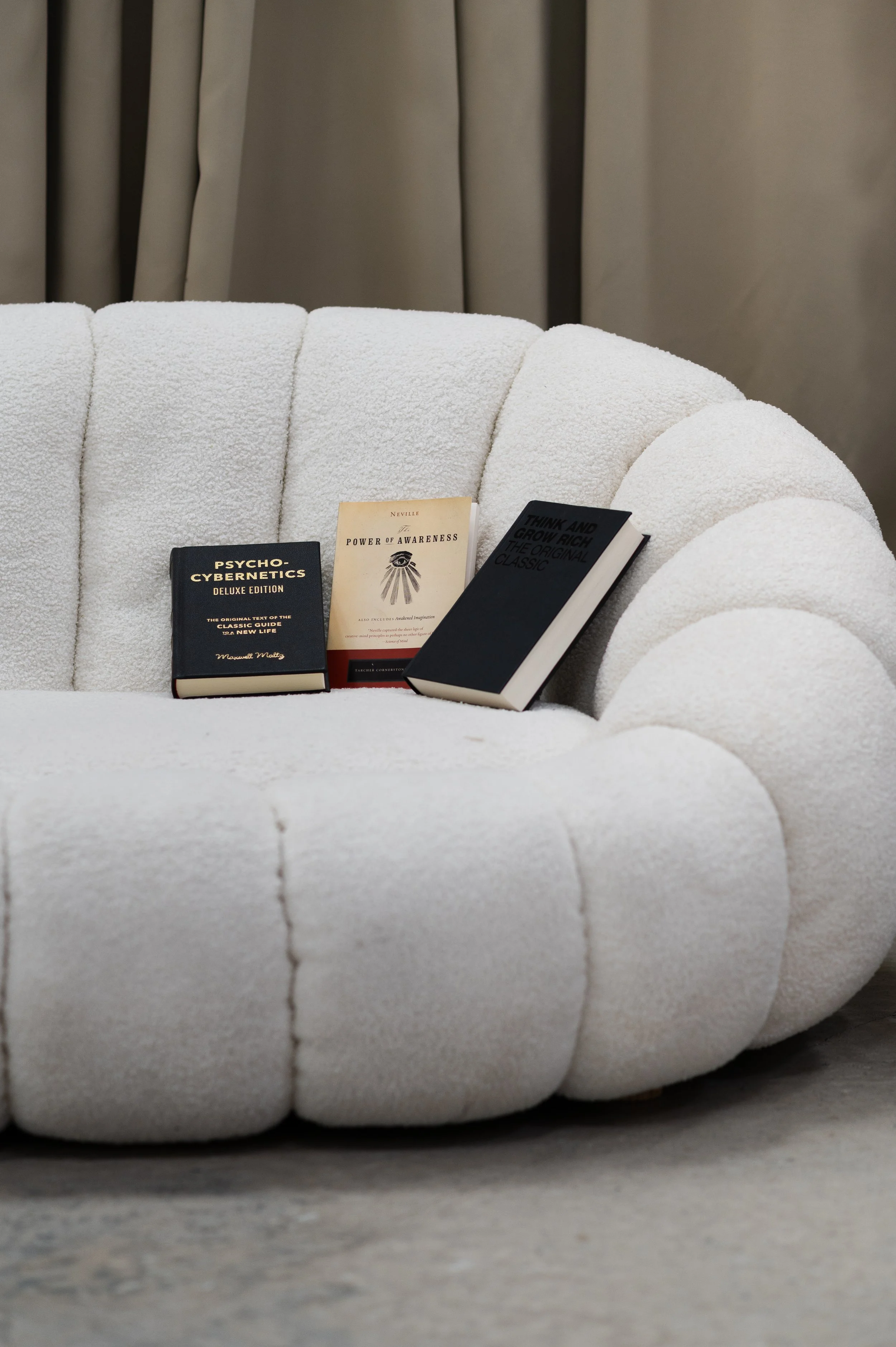 Three books resting on a plush white curved sofa.