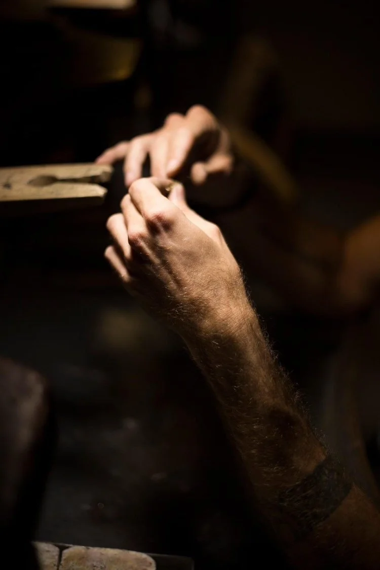 Close-up of a person's hands shaping or carving wood in a dimly lit workshop.