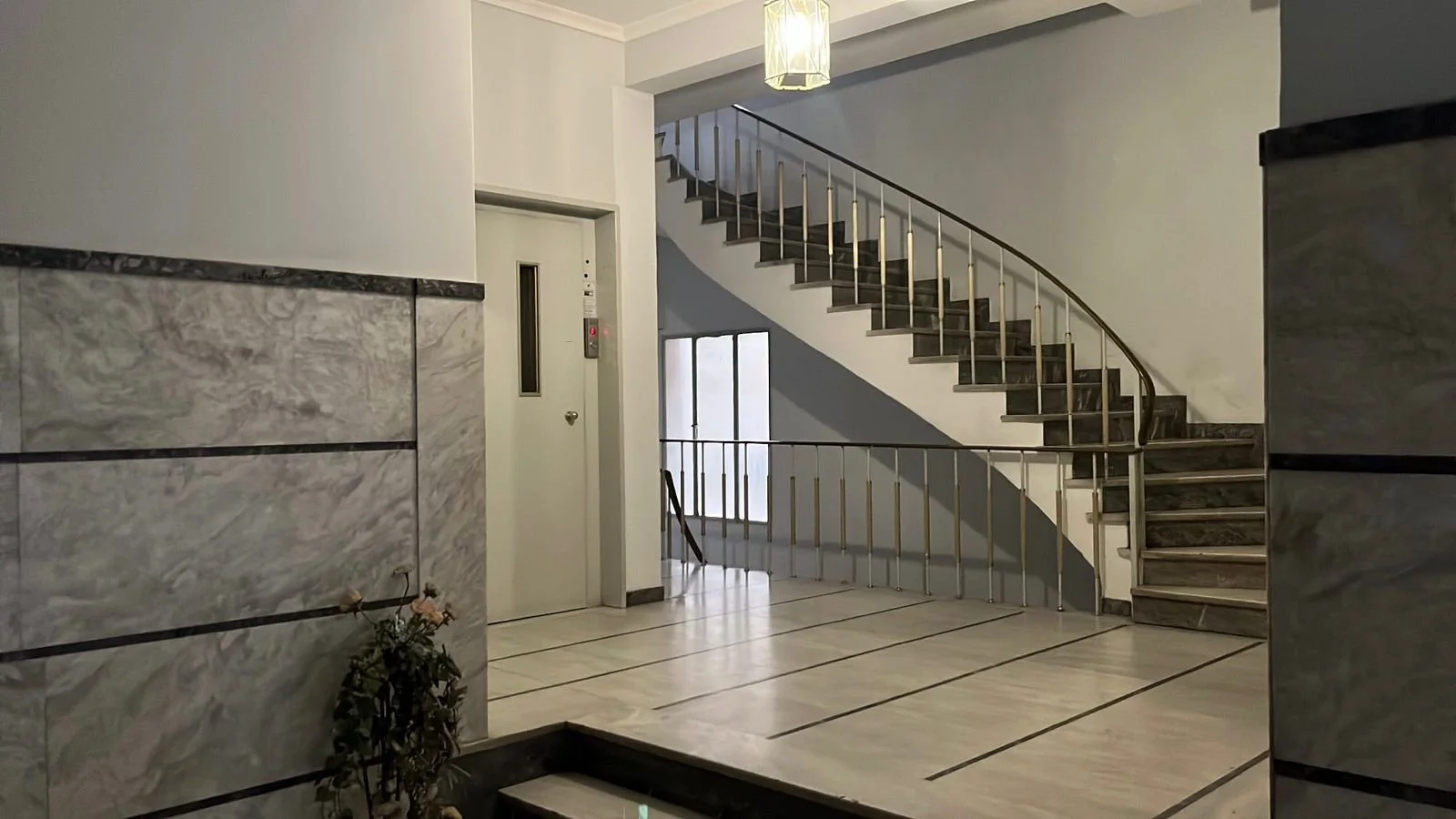 Interior view of a building lobby with a curved staircase, elevator, and marble walls.