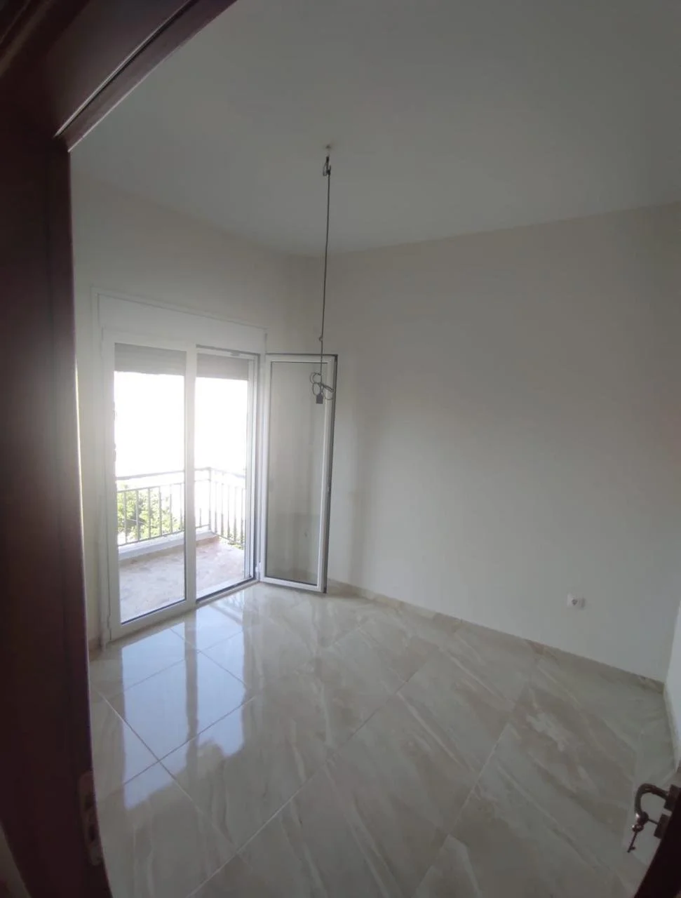Empty room with sliding glass door leading to a balcony, tiled floors, white walls, and a ceiling light fixture