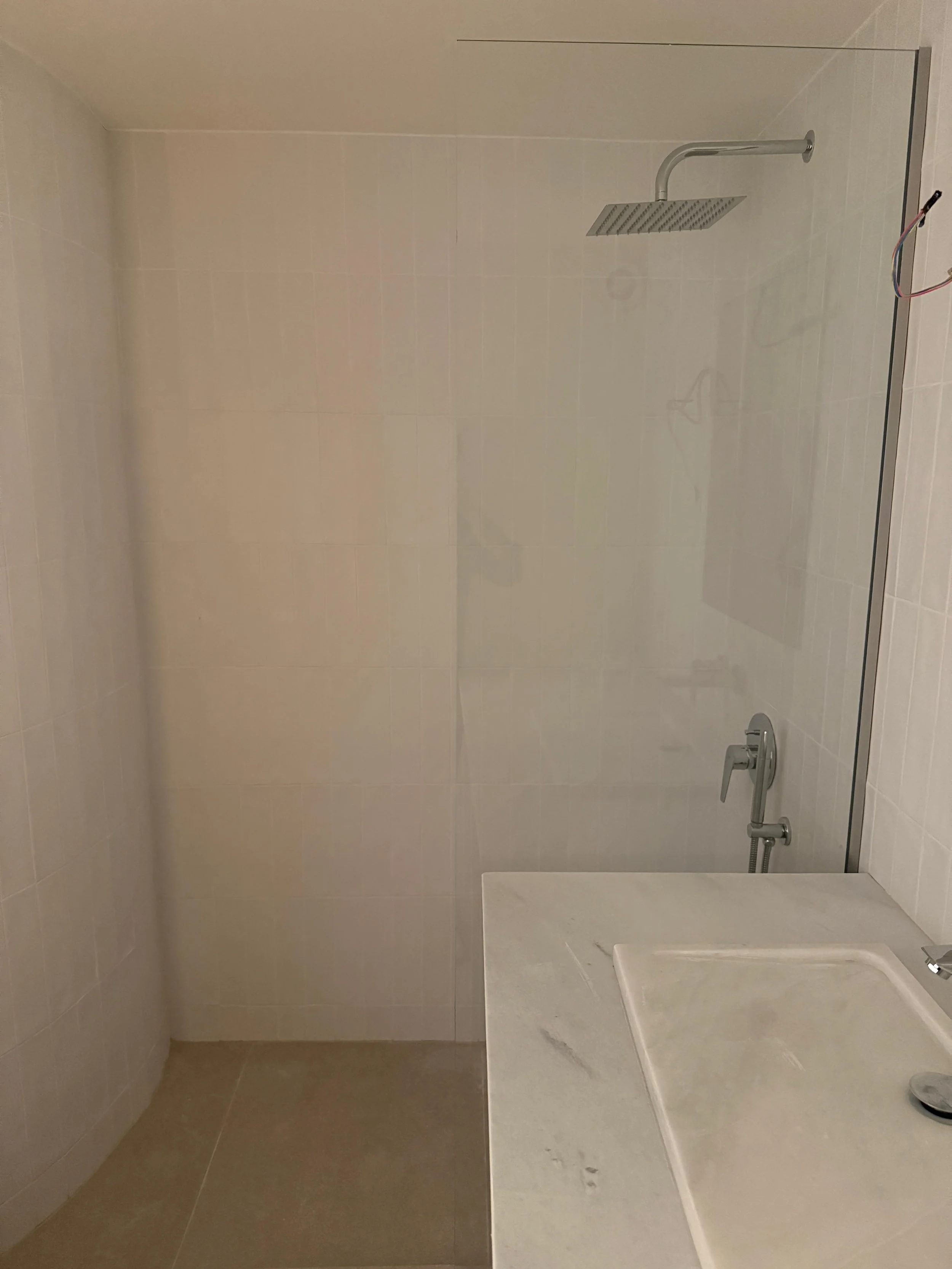 Empty shower with rain showerhead and a corner sink in a bathroom with beige tiles. Greece, Investment, Golden Visa, Real Estate, Cyprus, Georgia, Lebanon, LPI, Athens.