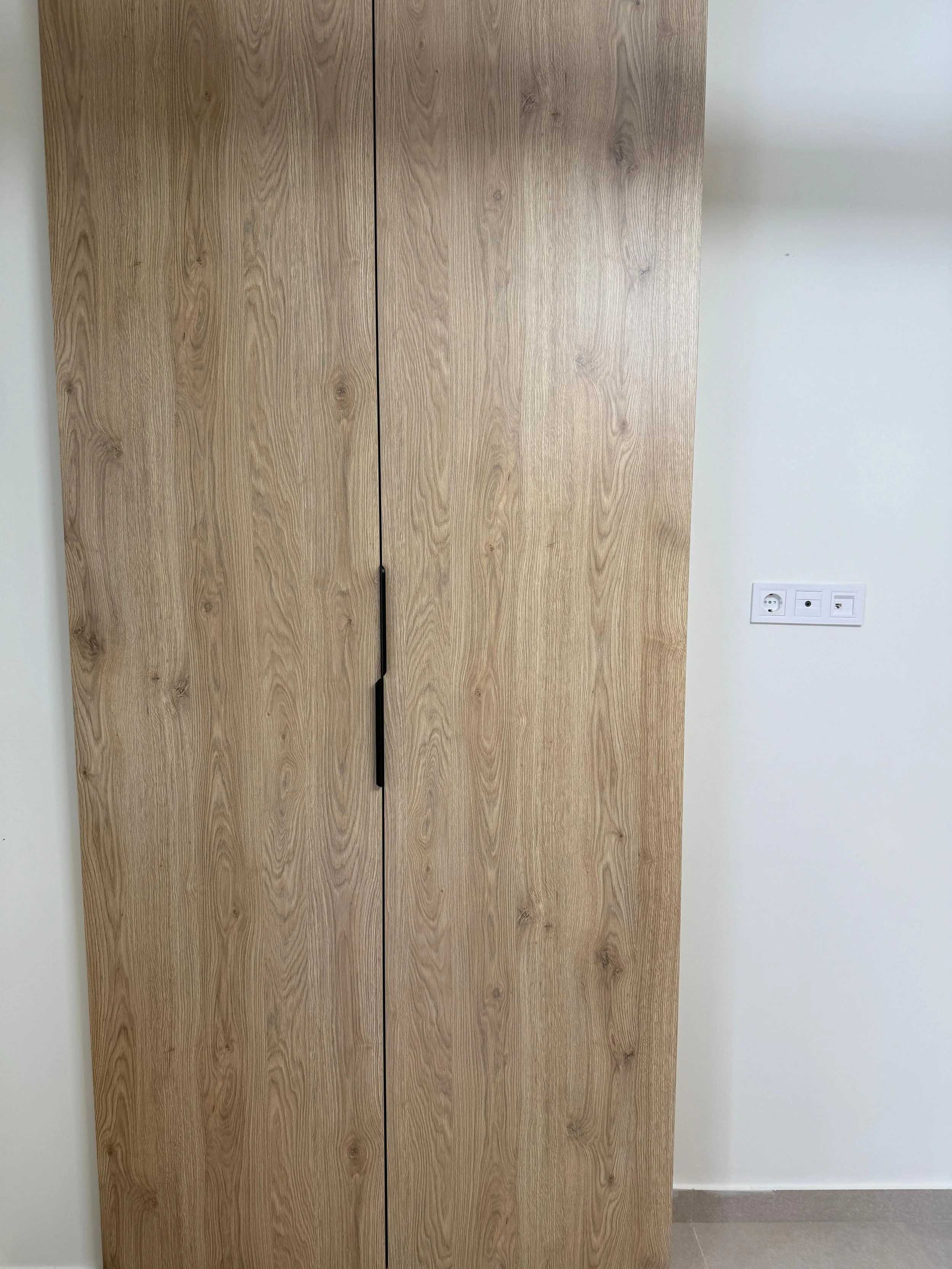 A tall wooden wardrobe in front of a white wall with a power outlet. Greece, Investment, Golden Visa, Real Estate, Cyprus, Georgia, Lebanon, LPI, Athens.