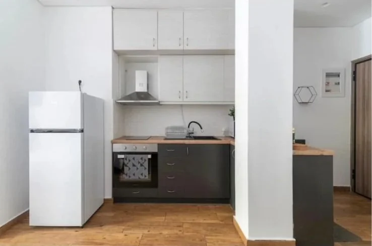 A small kitchen with white upper cabinets, gray lower cabinets, a wooden countertop, a white refrigerator, a stove with an oven, a range hood, a sink, and some wall decorations.