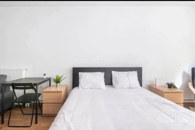 A bedroom with a bed, two bedside tables, a desk, and chairs, all against a plain white wall.