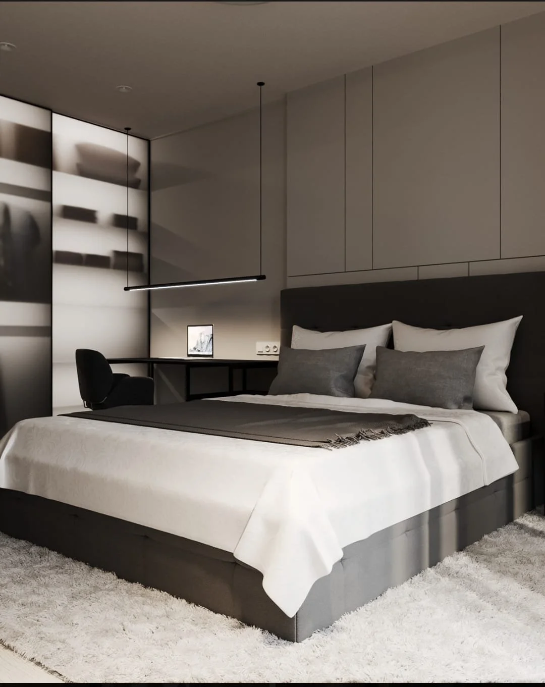 Modern bedroom with a neatly made bed featuring white and gray bedding and pillows, a black headboard, a fluffy white rug, and a small desk with a chair, a tablet, and sleek overhead lighting.