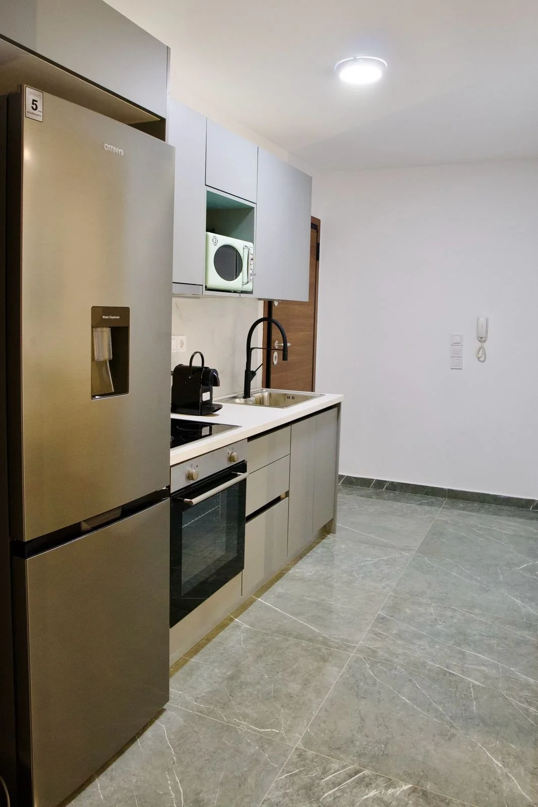 Modern minimalist kitchen with gray cabinetry, stainless steel refrigerator, oven, and microwave, black faucet, and tile flooring. Greece, Investment, Golden Visa, Real Estate, Cyprus, Georgia, Lebanon, LPI, Athens.