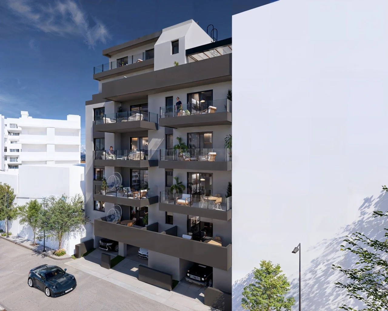 Modern multi-story apartment building with balconies, outdoor furniture, potted plants, and parked cars below. Clear blue sky overhead.