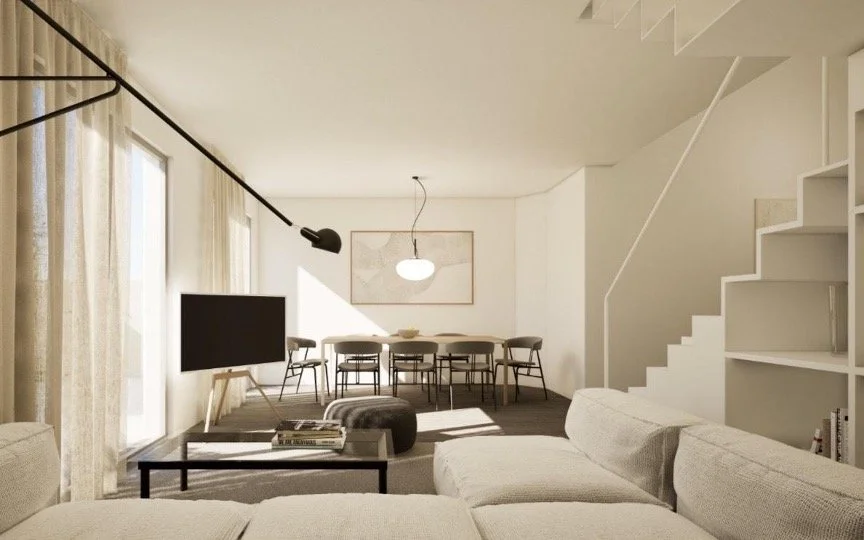 Open-concept living and dining room with white walls, a beige sofa, a flat-screen TV on a stand, a dining table with chairs, a hanging light fixture, and a staircase with built-in shelving.