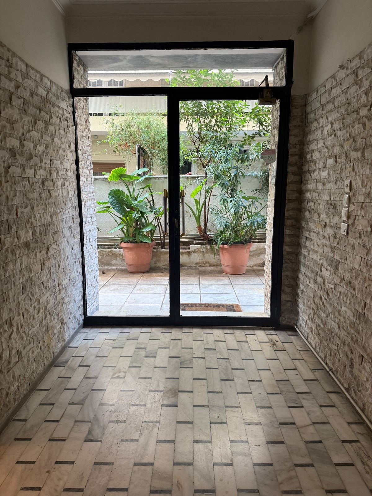 View through a glass sliding door leading to a small outdoor area with potted plants and greenery.