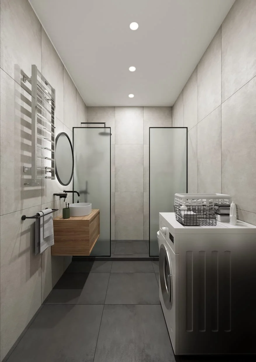 Modern bathroom with grey tiled walls and floor, a floating wooden vanity with a vessel sink and round mirror, a towel rack, a glass shower enclosure, and a washing machine with a laundry basket on top.