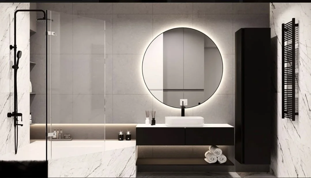 Modern bathroom with a round backlit mirror, white sink, black cabinet, and a wall-mounted towel rack.