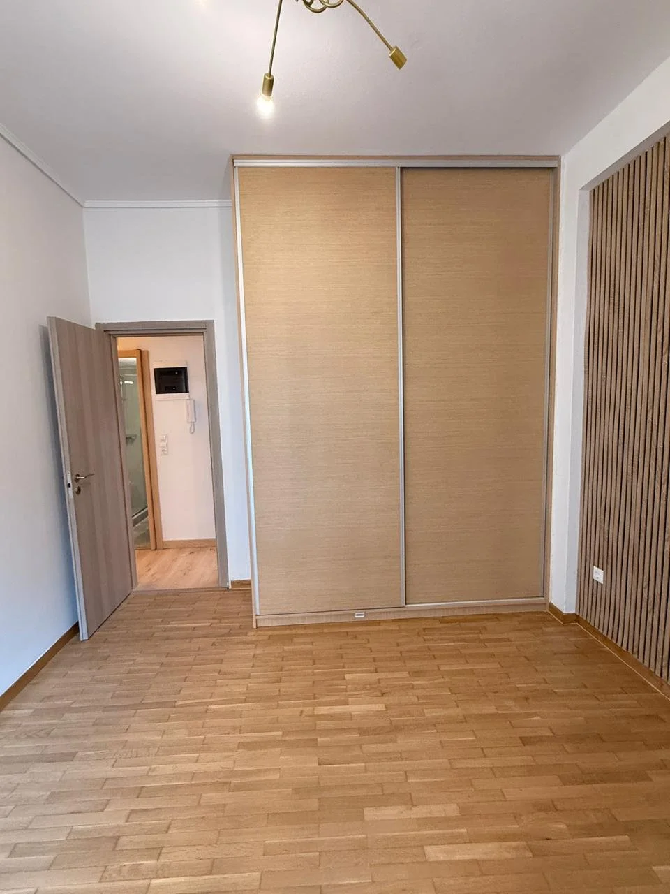 Empty room with wooden flooring, a sliding door wardrobe, and an open door leading to a bathroom or hallway.