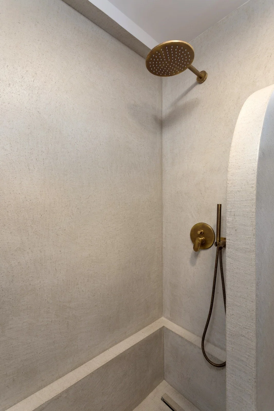 Brass showerhead and handles in a minimalist shower with beige textured walls.