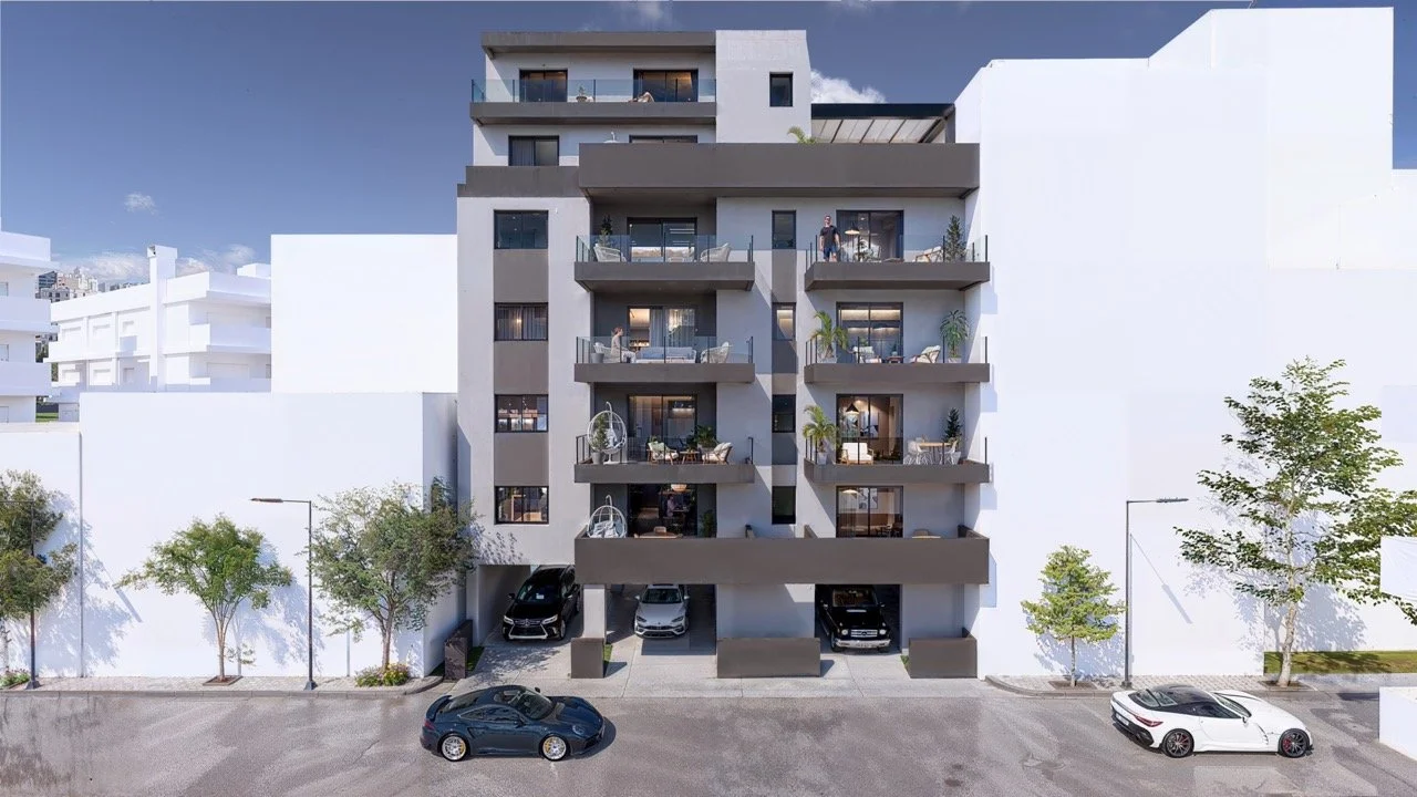 Modern multi-story residential building with balconies, cars parked underneath, and trees flanking the street in front.