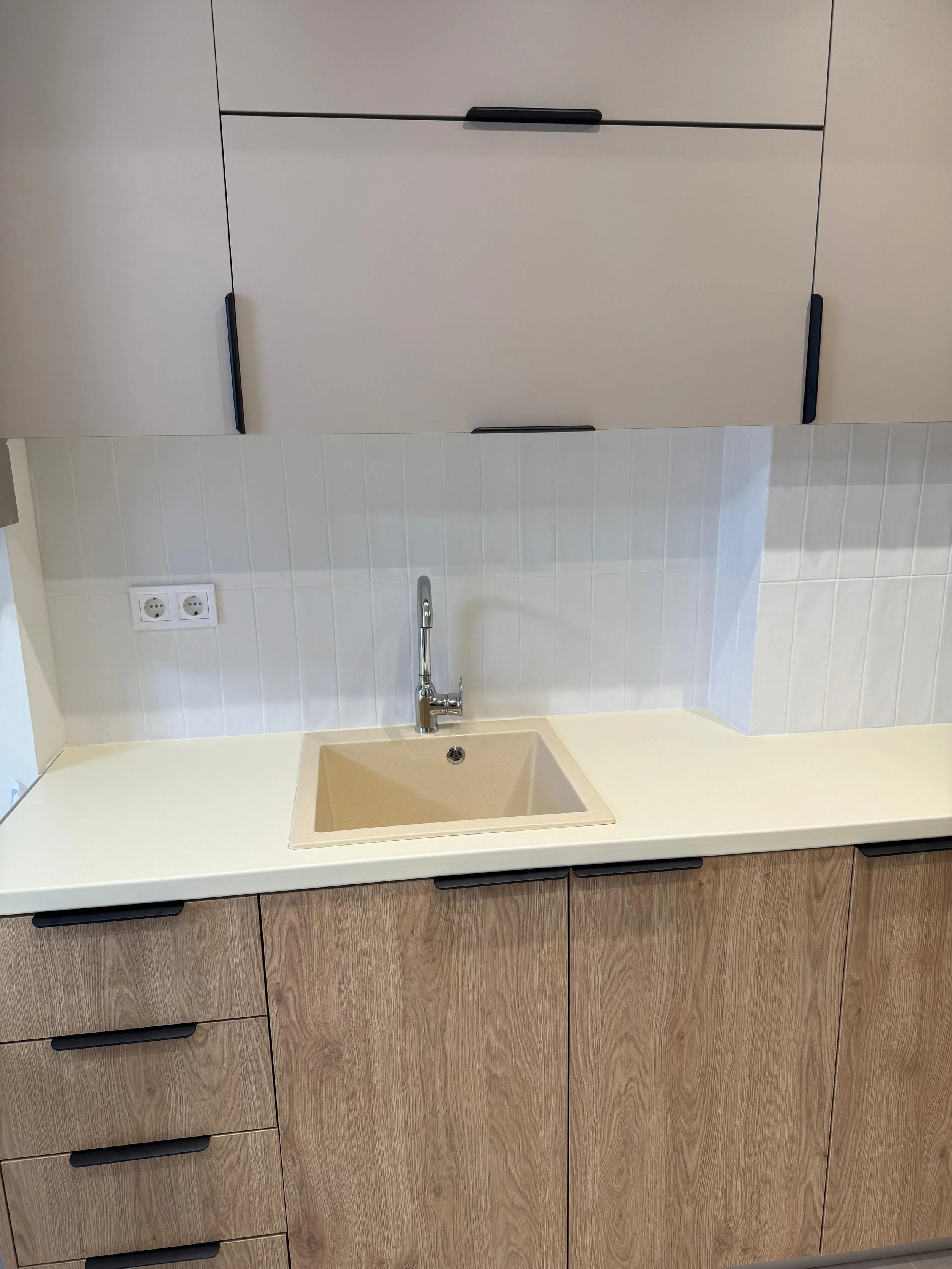Kitchen countertop with sink, faucet, and beige cabinetry above and below. White tiled backsplash and electrical outlets are visible. Greece, Investment, Golden Visa, Real Estate, Cyprus, Georgia, Lebanon, LPI, Athens.