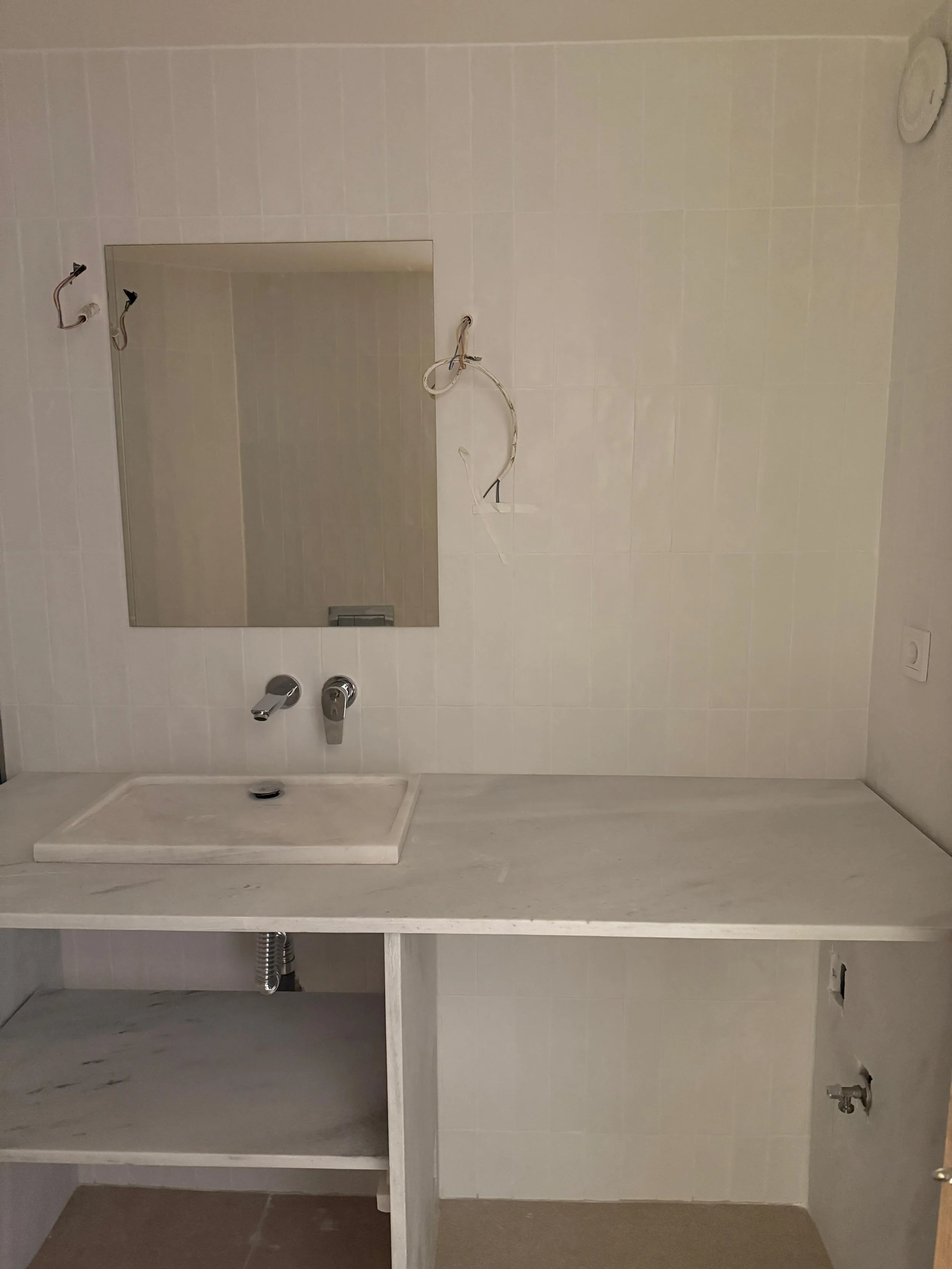 A partially finished bathroom vanity area with a mirror, sink, and exposed plumbing, with electrical wiring hanging from the wall. Greece, Investment, Golden Visa, Real Estate, Cyprus, Georgia, Lebanon, LPI, Athens.