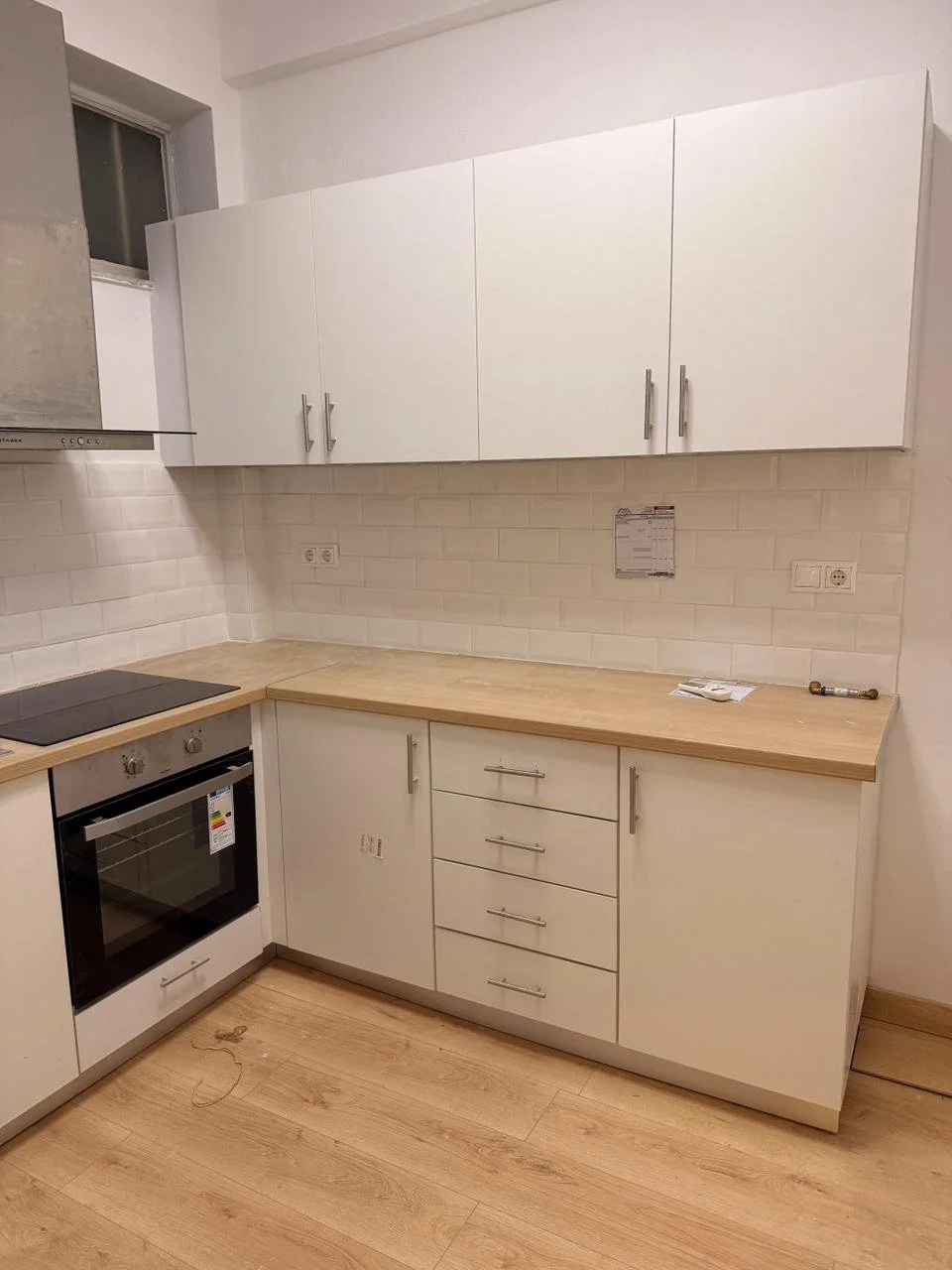 Empty modern kitchen with white cabinets, wooden countertop, and white subway tile backsplash.