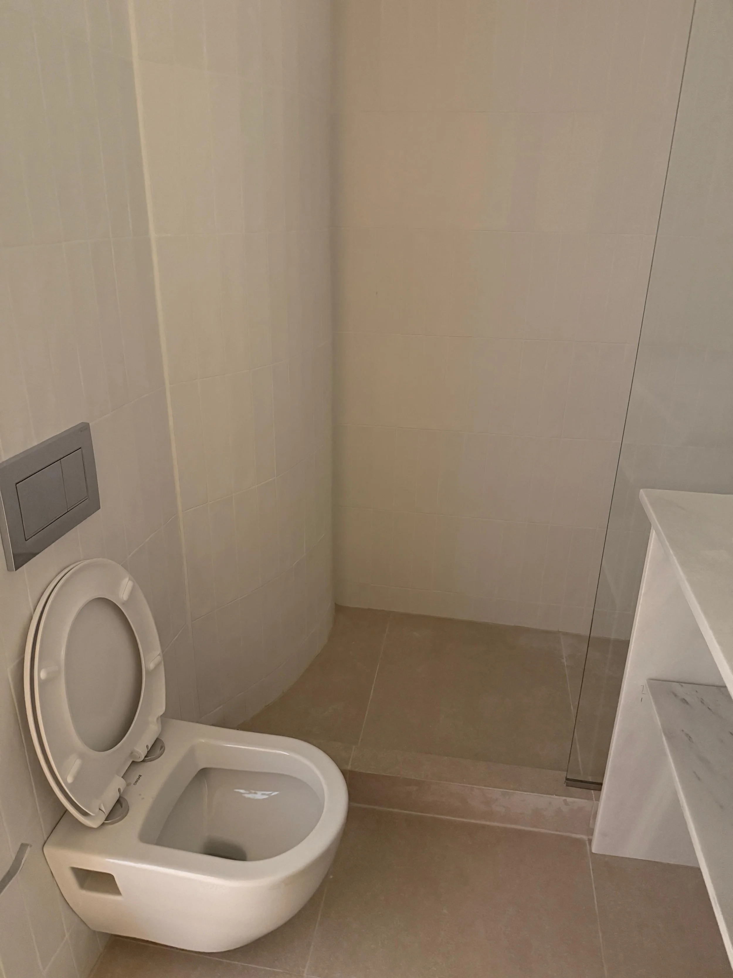 Modern bathroom with a wall-mounted toilet, beige tiled walls and floor, and a white marble countertop. Greece, Investment, Golden Visa, Real Estate, Cyprus, Georgia, Lebanon, LPI, Athens.